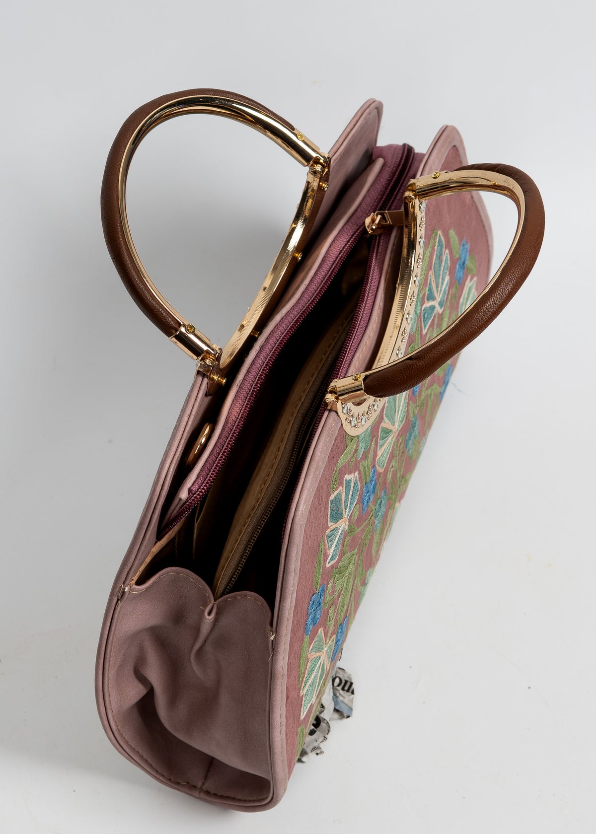 Top angled view of the mauve handbag, showing its zip opening, folded side panel and circular gold-toned handles