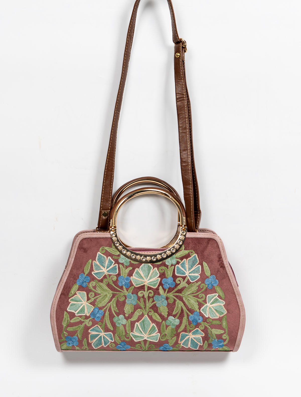 Mauve embroidered handbag hanging from a long brown strap, with circular handles above the green-and-blue leaf-and-flower panel