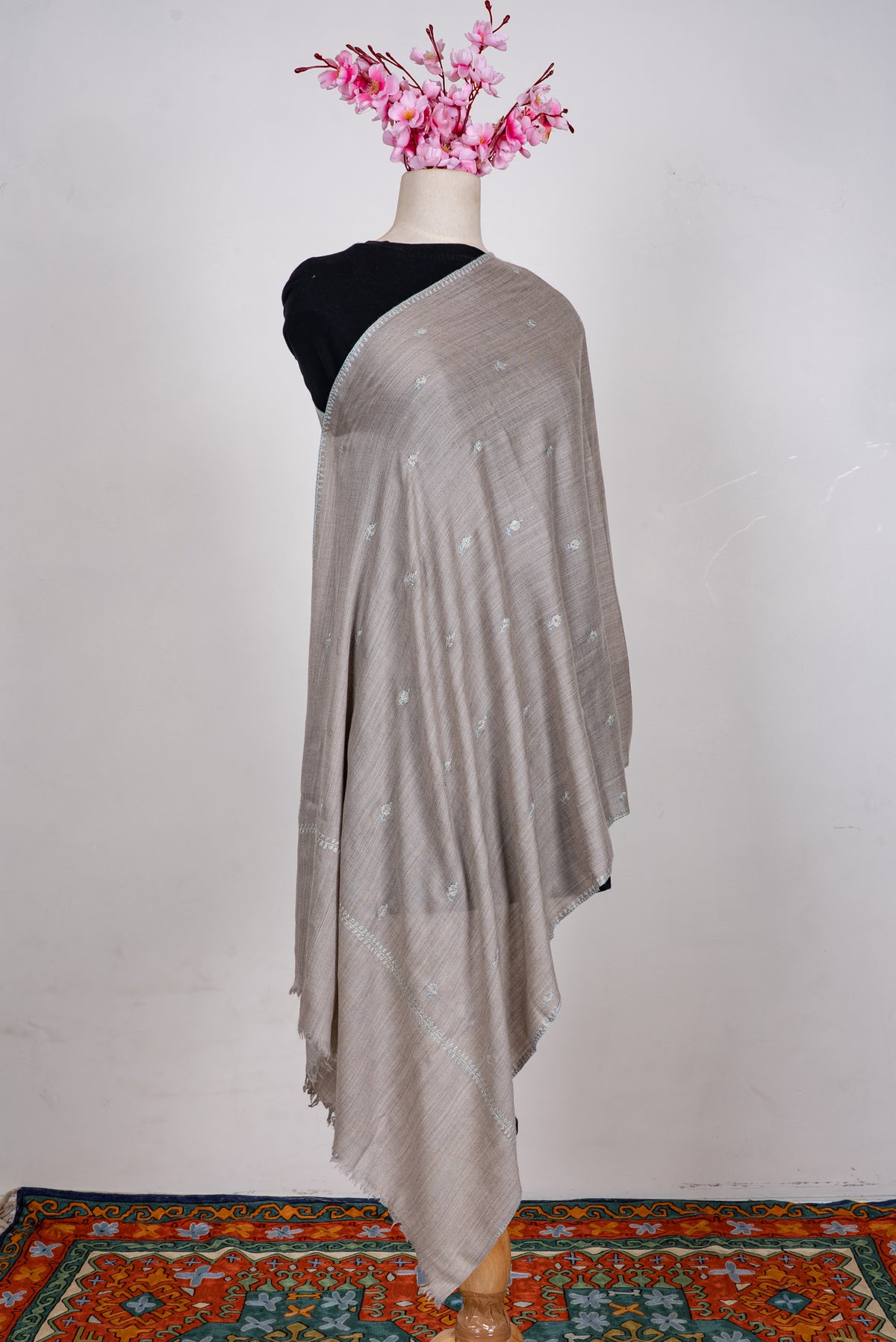 Full-length dove-grey scarf draped over one shoulder, with scattered pale embroidered sprigs and a narrow border