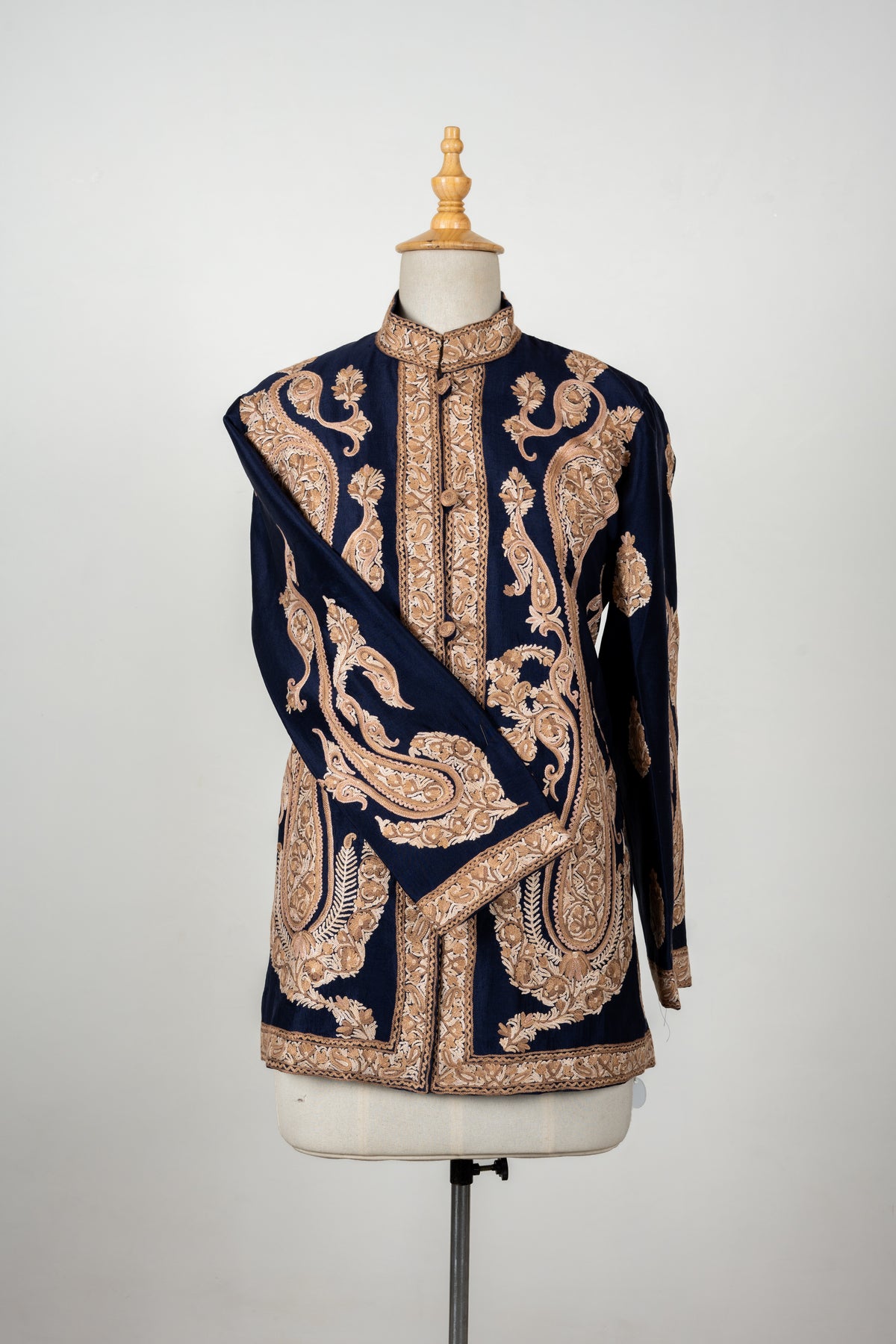 Front of a navy raw silk jacket with large beige Aari paisleys, a stand collar and a sleeve folded across the buttoned front