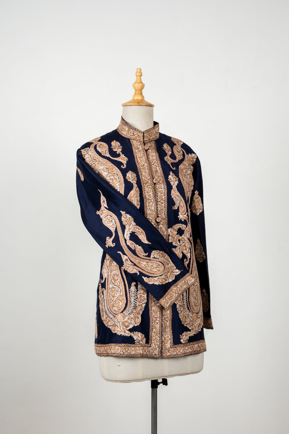 Angled navy short jacket on a mannequin with beige Aari paisleys, embroidered front borders and one sleeve crossed