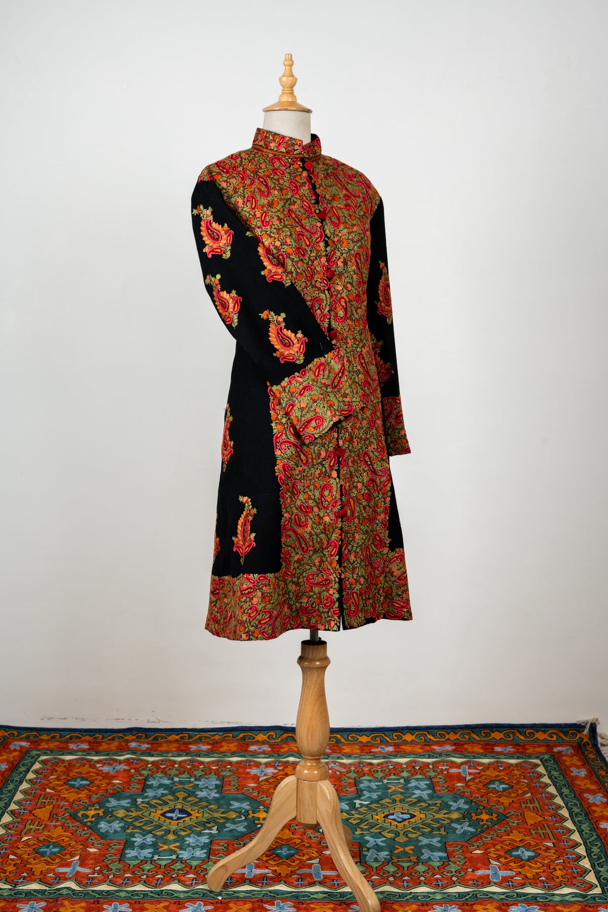 Full-length view of the black jacket on a mannequin, showing red paisley motifs on the sleeve beside the dense embroidered front.