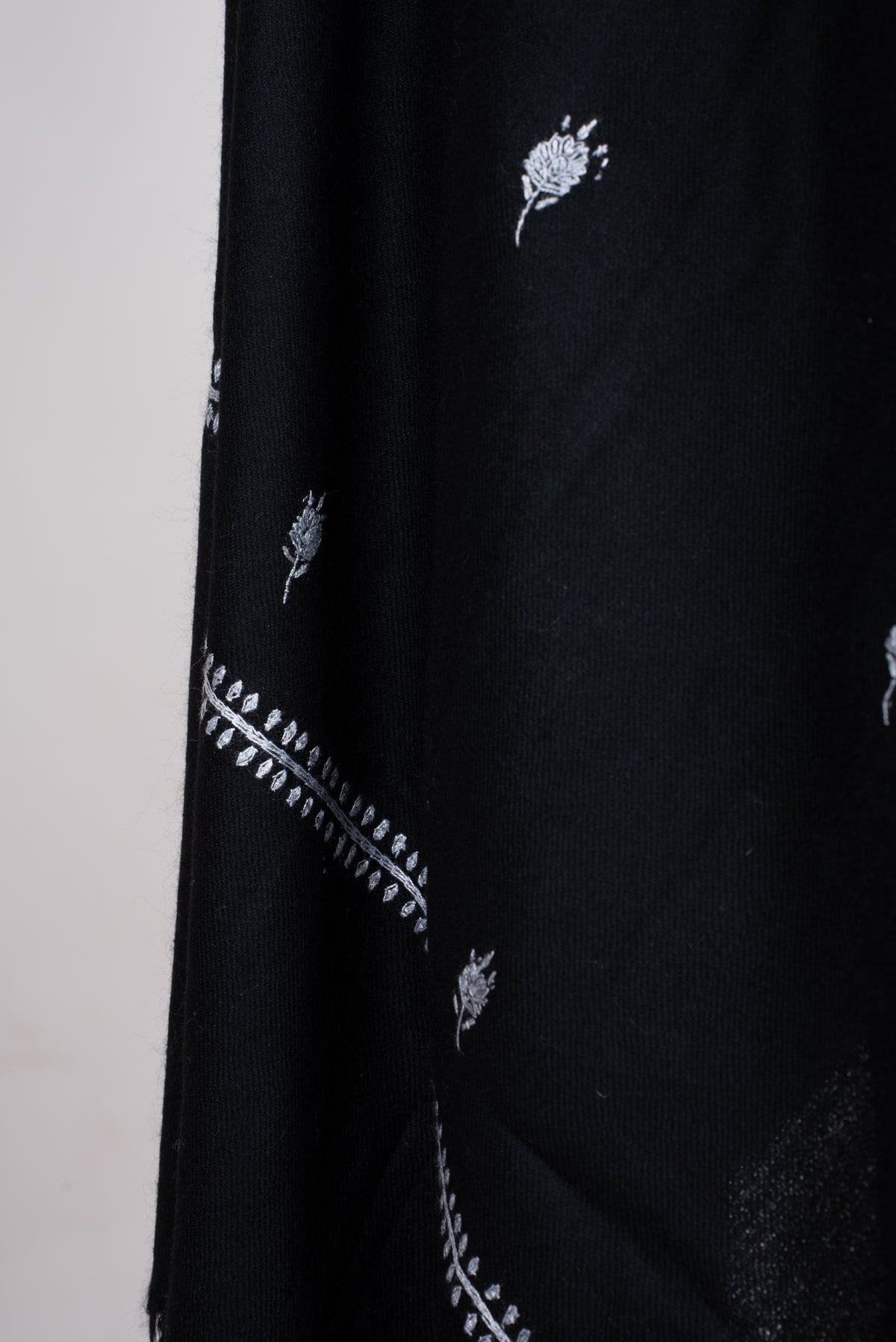 Draped black scarf detail with small white embroidered flower sprigs and a fine white leafy border.