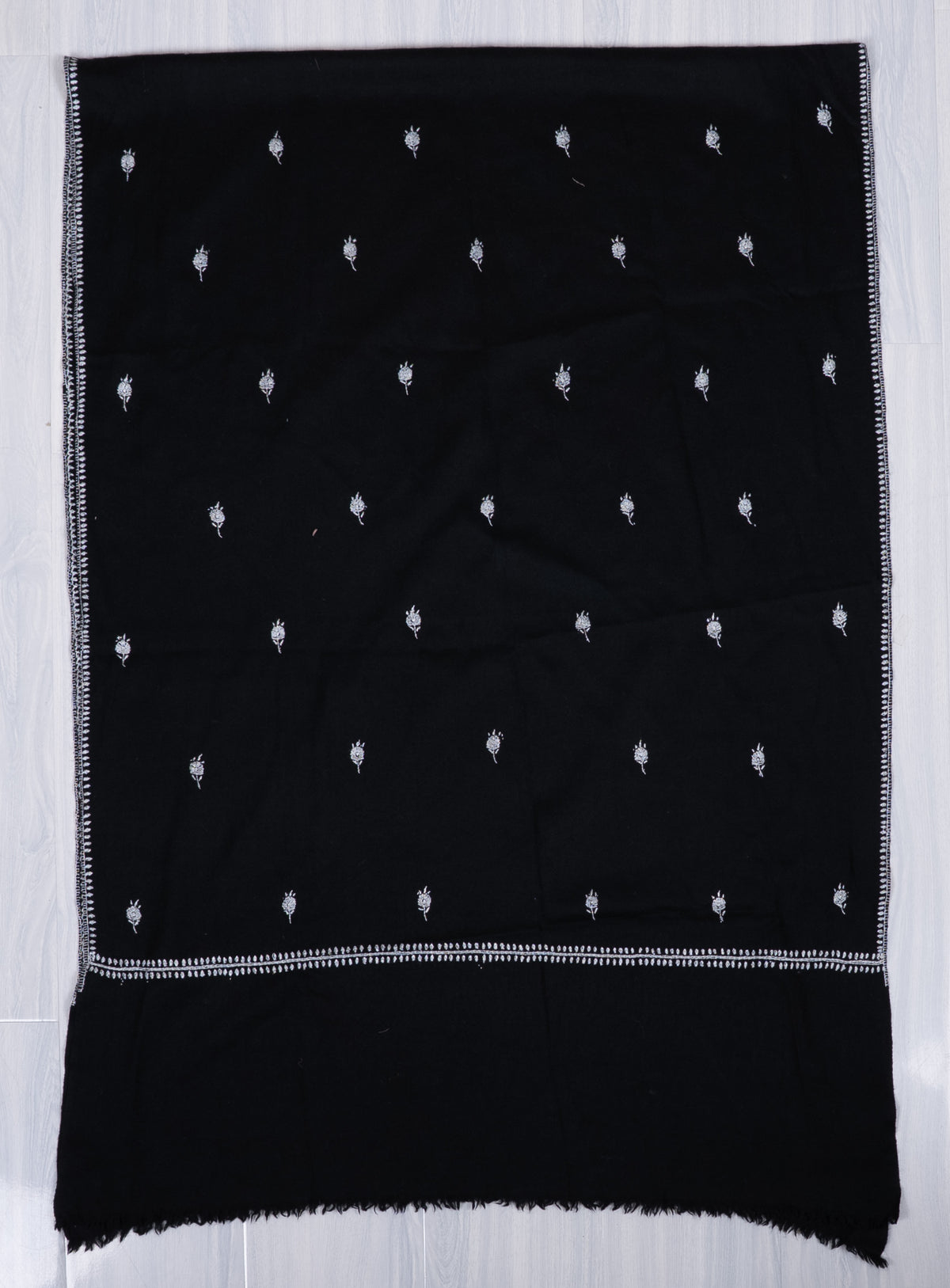 Black scarf laid flat lengthwise, with rows of small white embroidered floral motifs, narrow borders and a wide plain end.