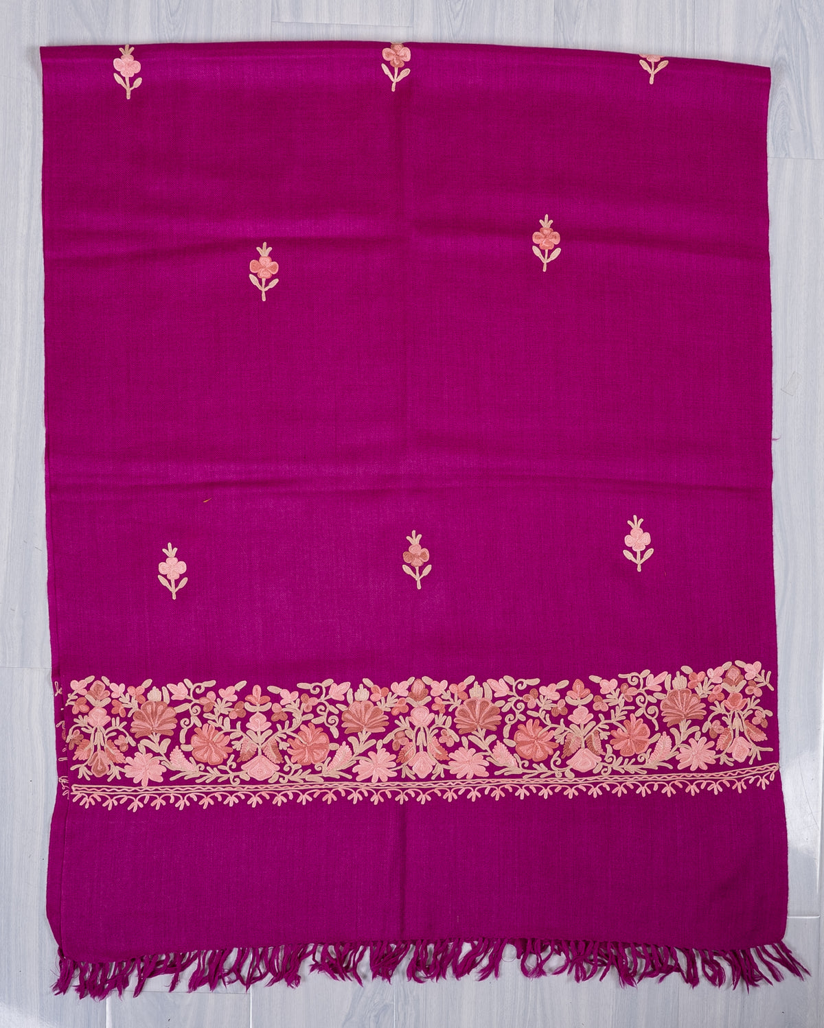 Magenta scarf spread flat, showing scattered pale floral sprigs and a blush-and-beige embroidered border above a fringed end