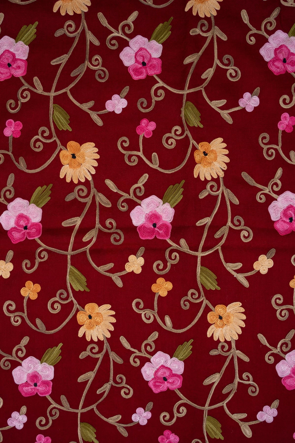 Close-up of pink and golden Aari flowers linked by pale curling stems across maroon shawl