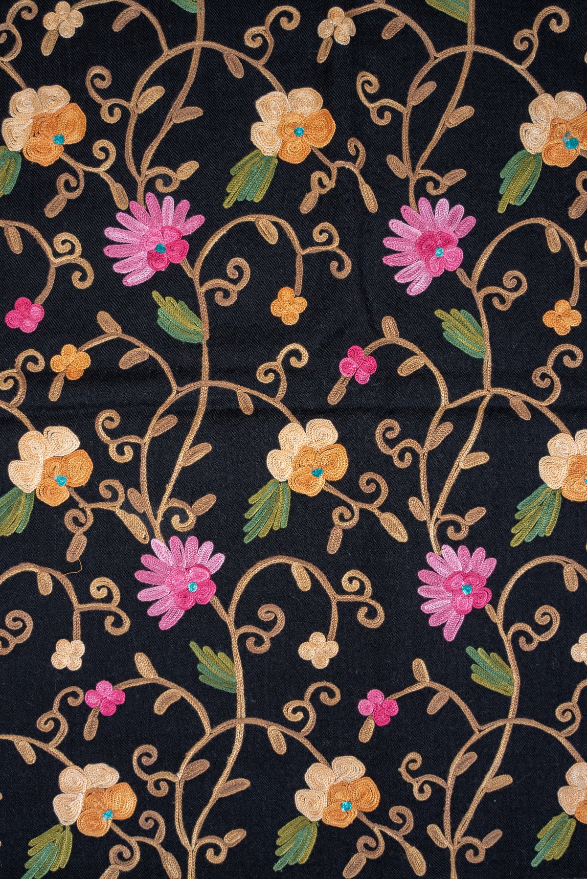 Close-up of repeating pink and cream Aari flowers with green leaves and curling tan stems on a black shawl.
