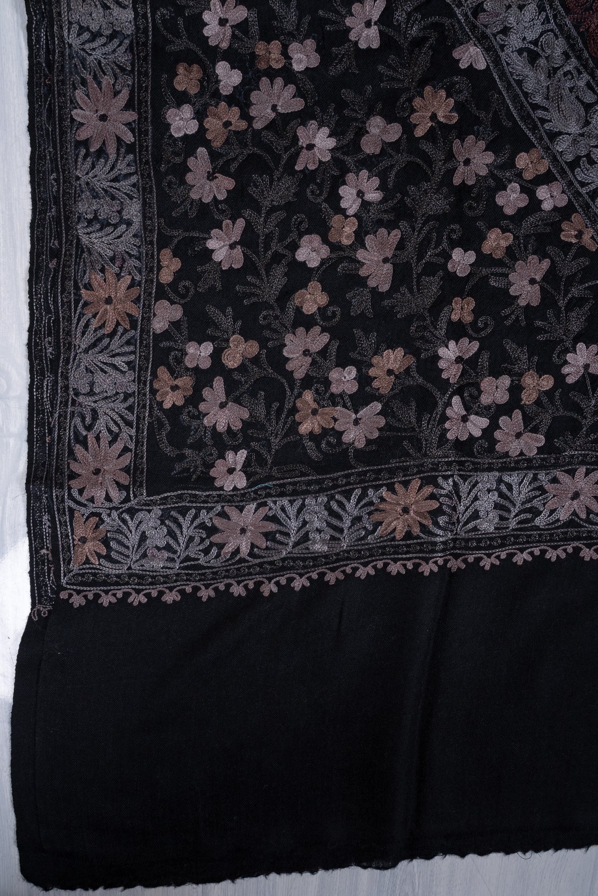 Corner detail of black shawl with muted-rose flowers, grey leafy borders and a plain black end