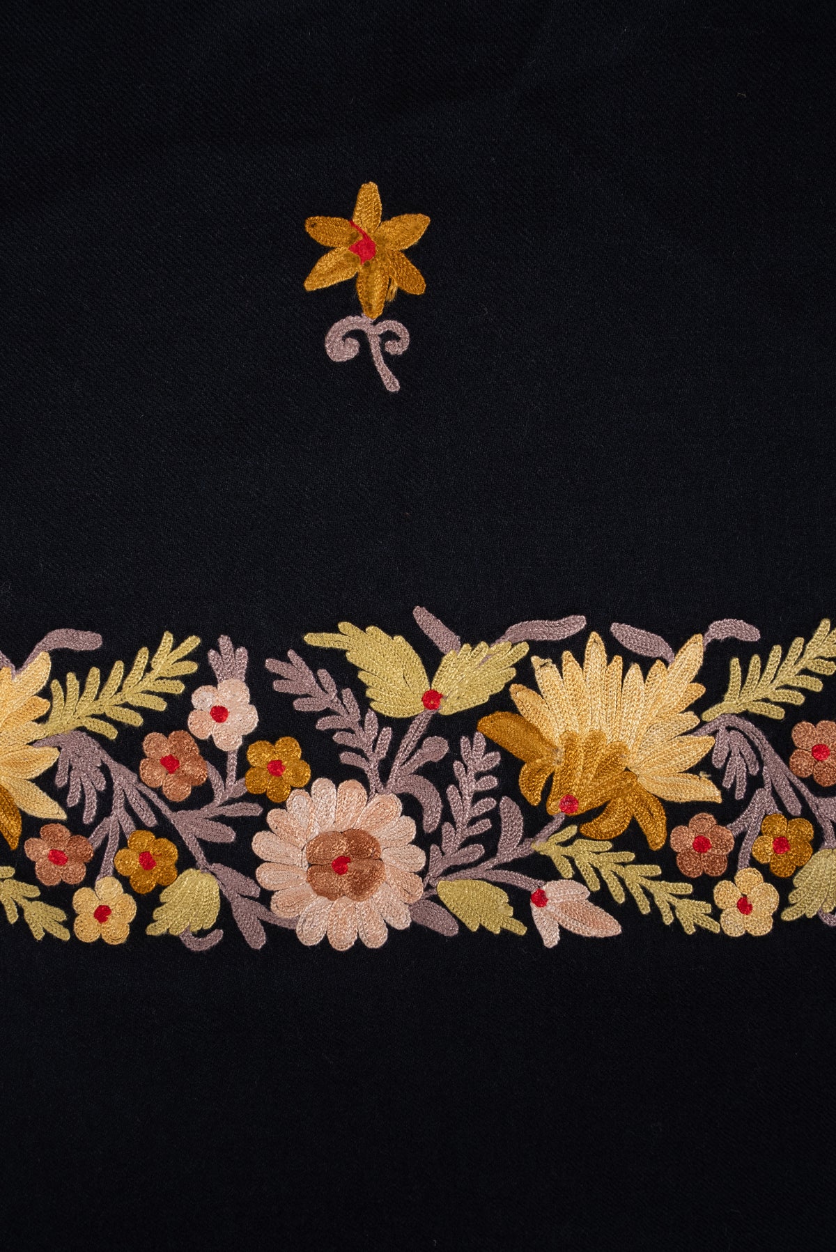 Detail of a small yellow Aari flower above the cream, yellow and pale pink floral border on the black shawl