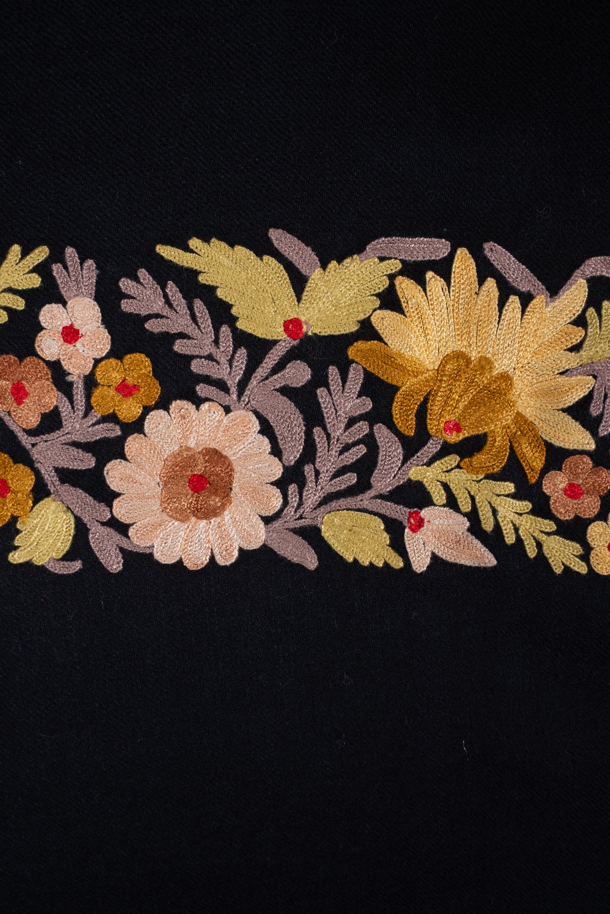 Close-up of the black shawl’s Aari border, with cream and yellow flowers, red centres and pale pink leafy stems