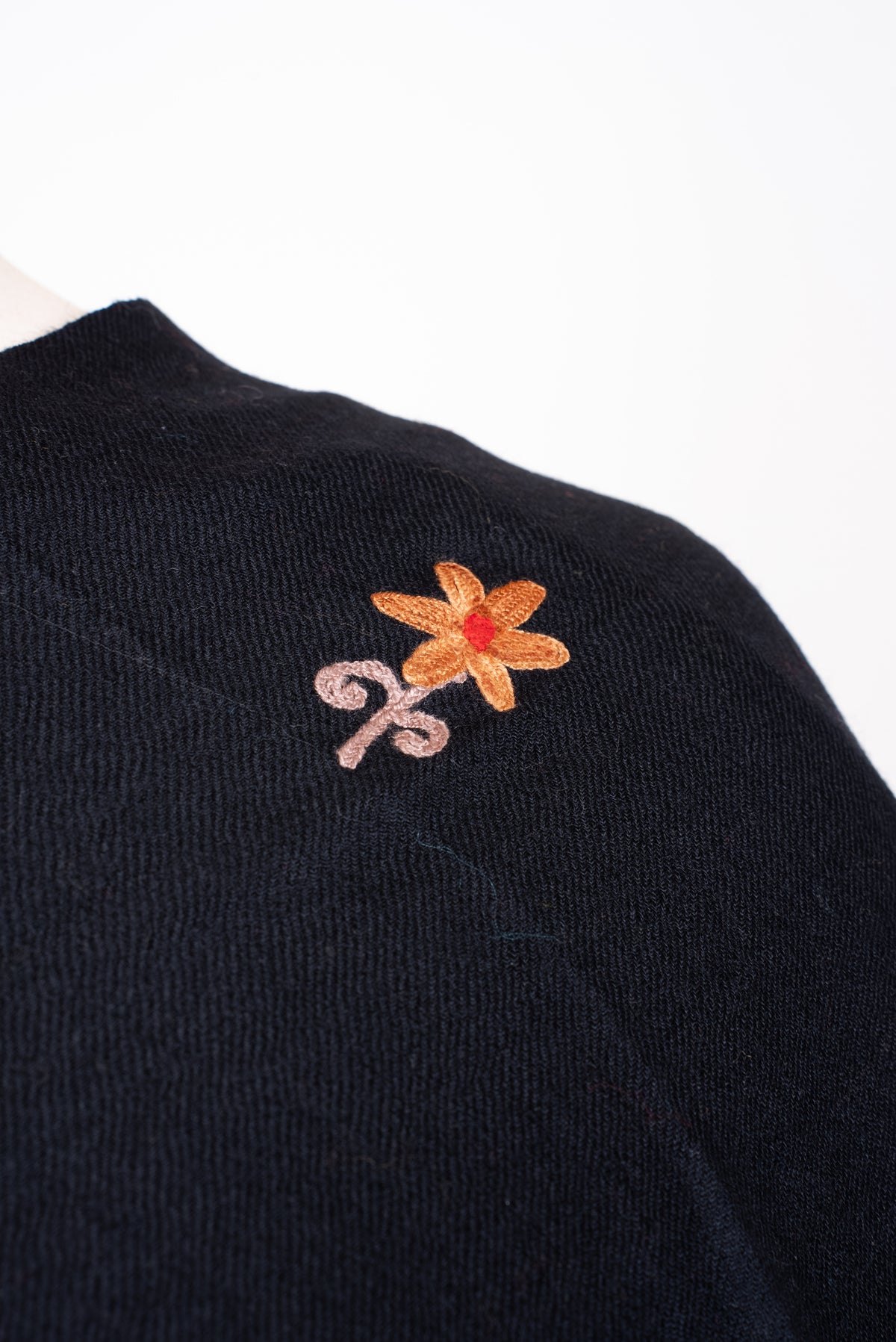 Shoulder close-up of the black shawl, with a small orange-yellow Aari flower and curling pale pink stem