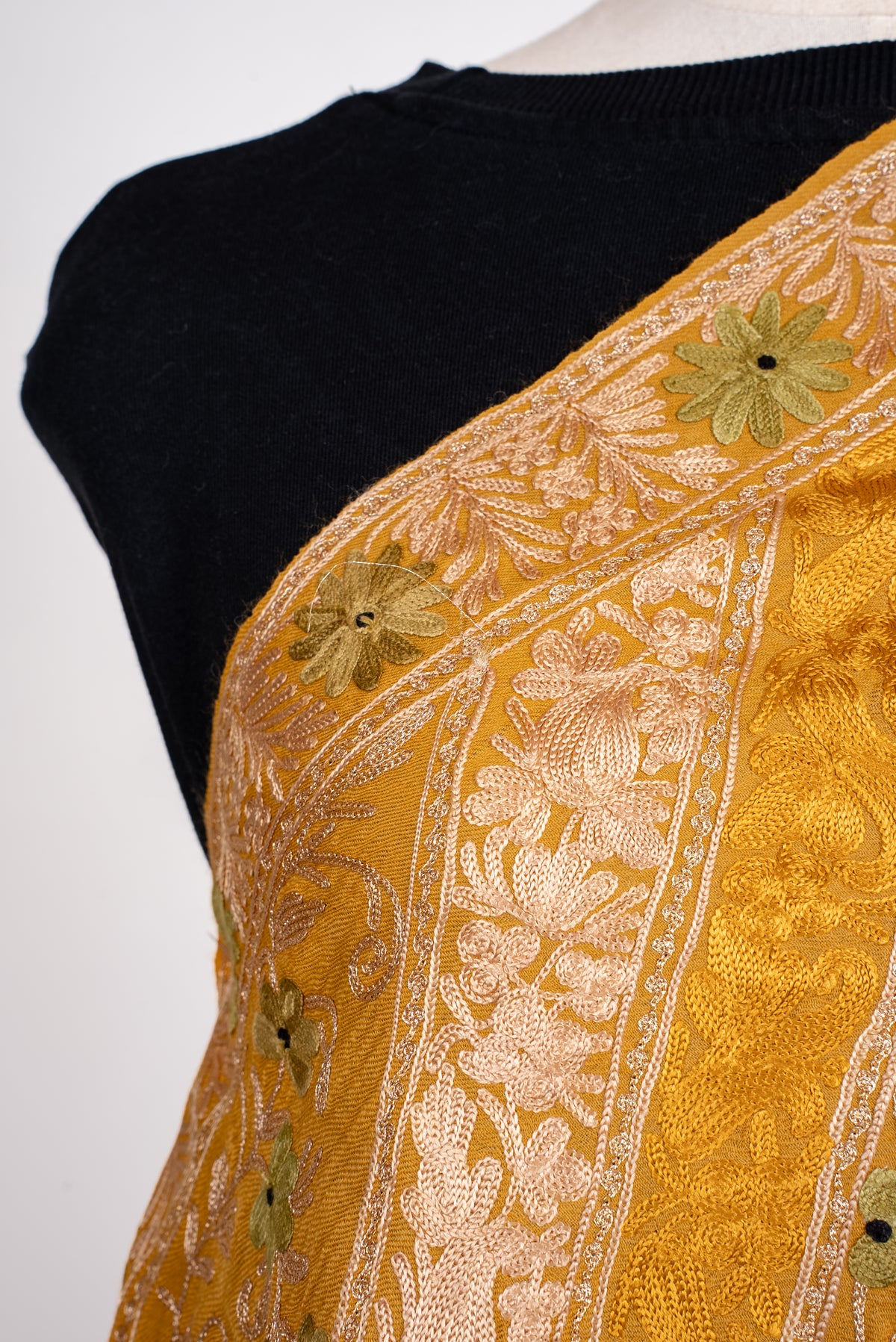 Shoulder close-up of the mustard shawl, showing pale Aari floral bands and olive-green flowers with dark centres