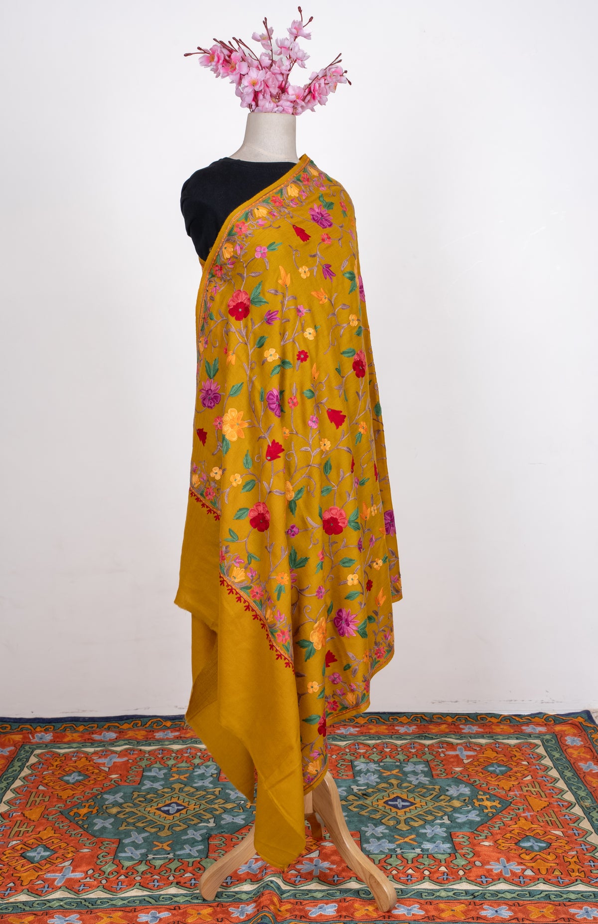 Full-length mustard shawl draped over one shoulder, with colourful floral vines, patterned borders and a plain end