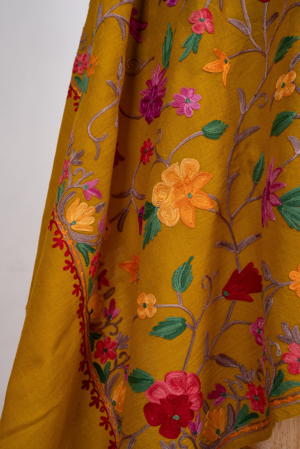 Close-up of mustard shawl folds with red, pink and yellow Aari flowers, green leaves and pale curling stems