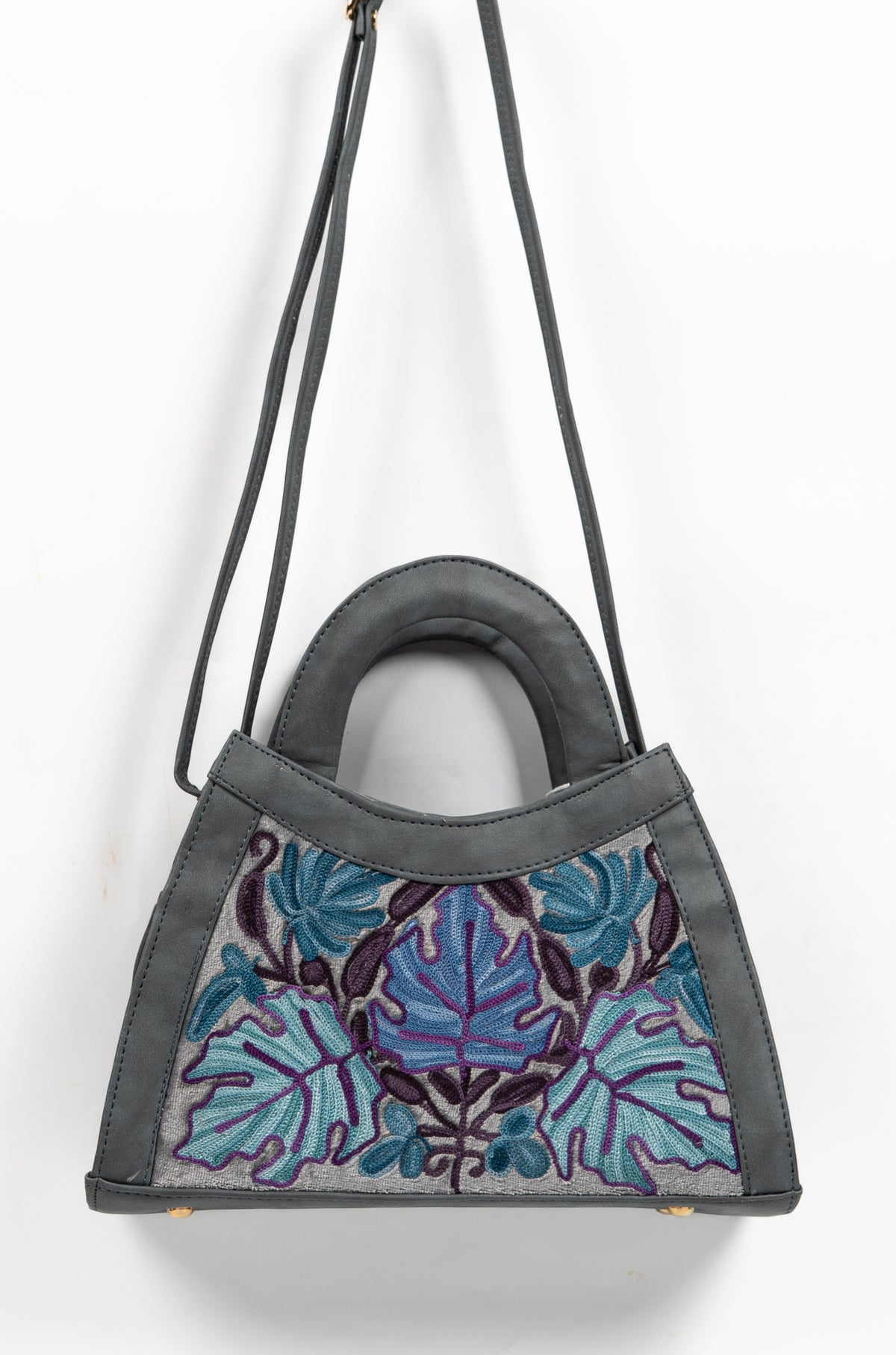 Grey embroidered handbag hanging from its long shoulder strap, showing blue leaf motifs across the front panel.