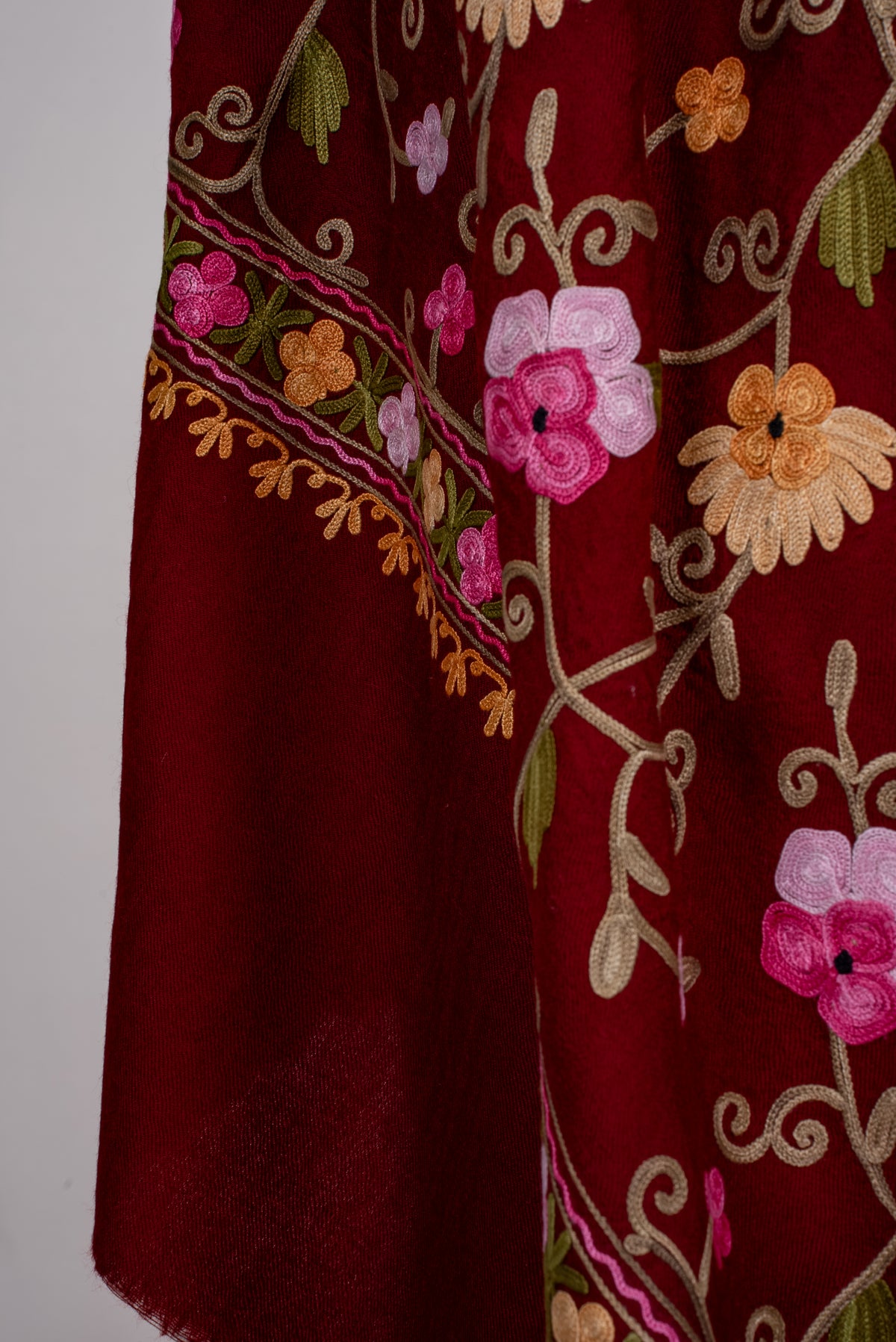 Close-up of maroon shawl folds with pink and golden flowers, pale stems and a narrow floral border