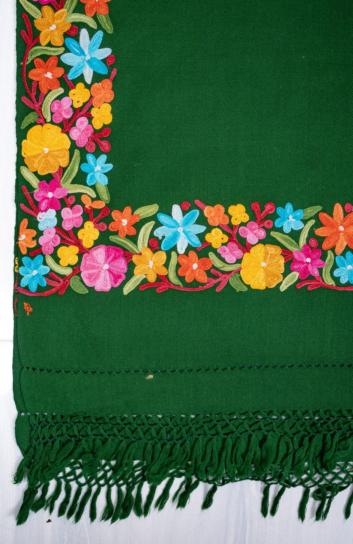 Flat corner detail of the forest-green shawl, with pink, yellow and blue Aari flowers above green knotted fringe