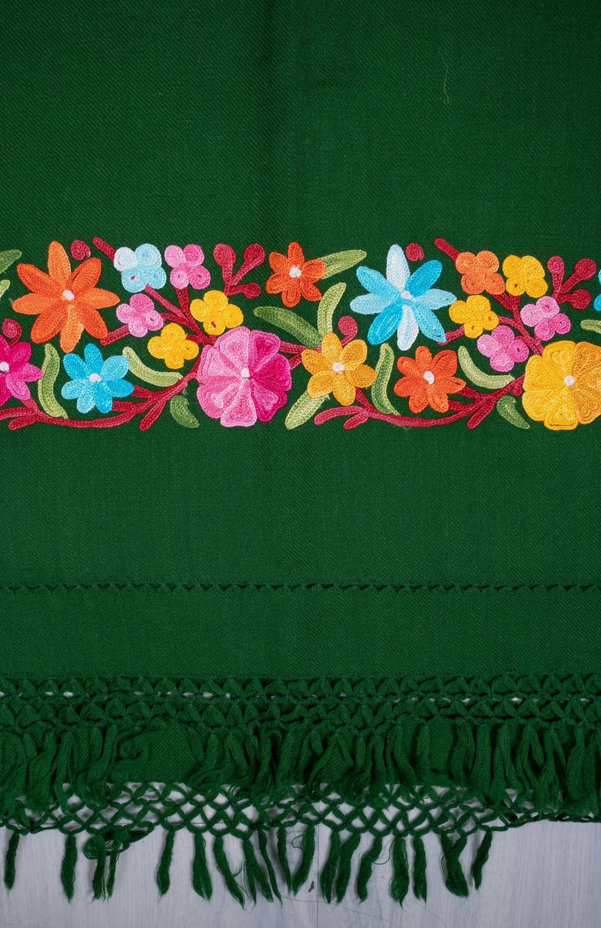 End-border detail of the green shawl, with bright pink, yellow, blue and orange Aari flowers above matching knotted fringe