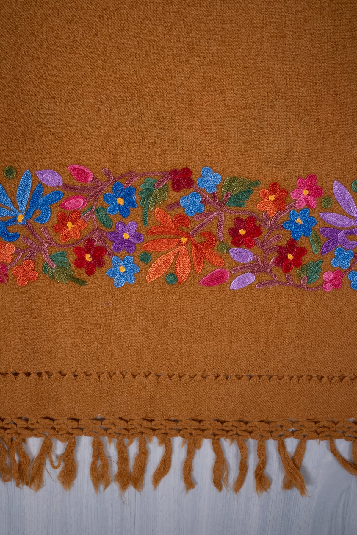 Close-up of the mustard shawl’s multicoloured Aari floral end border above an openwork strip and knotted fringe