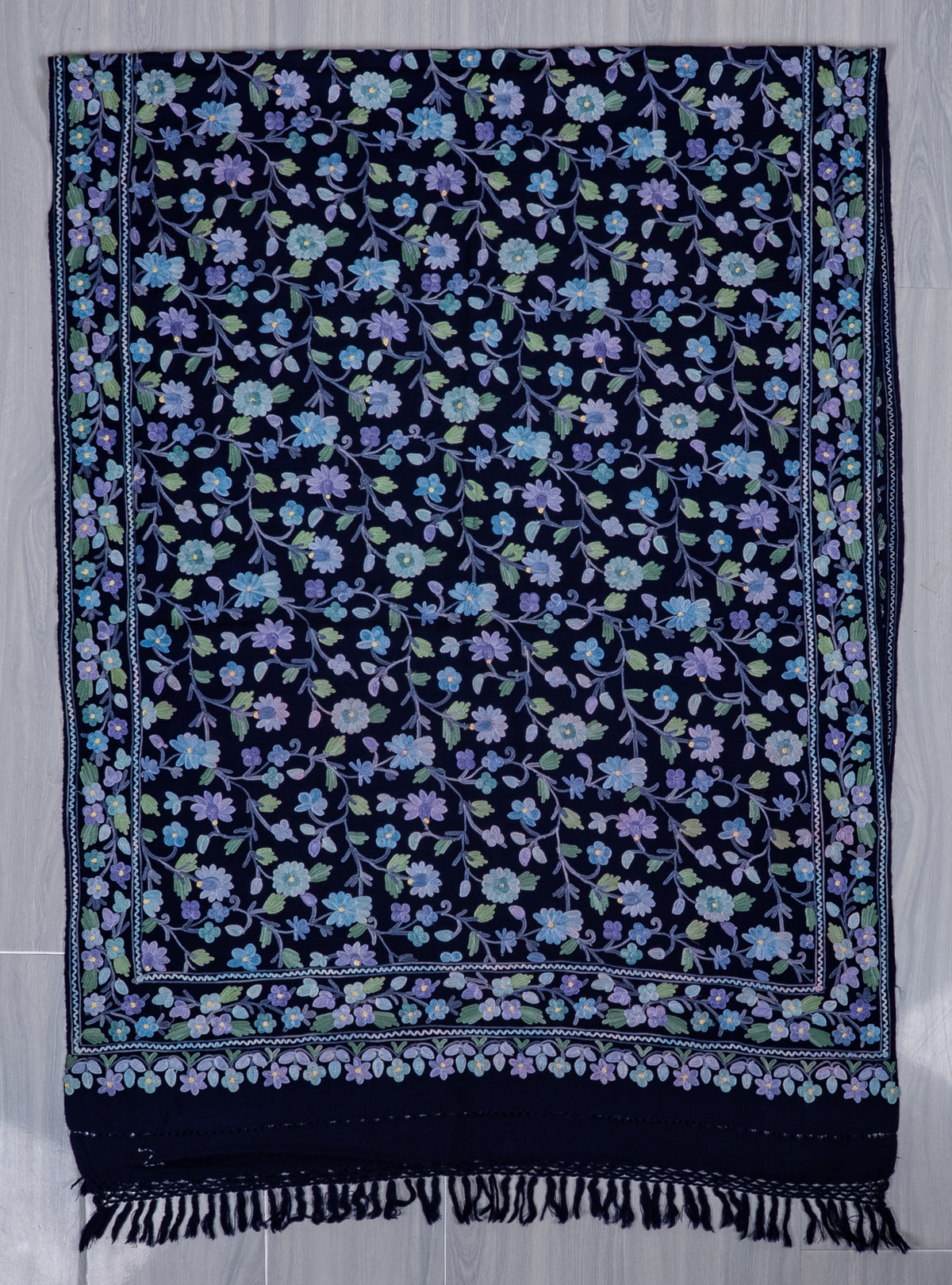 Sapphire-blue shawl spread flat, with pastel Aari floral vines, a layered floral border and a dark fringed end
