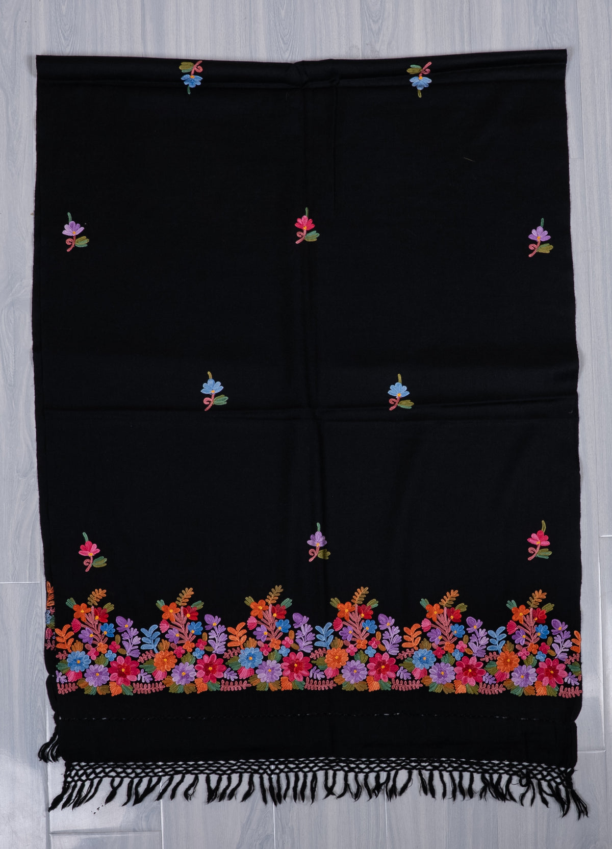 Black shawl laid flat lengthwise, with small scattered floral sprigs, a multicoloured Aari flower border and knotted black fringe.