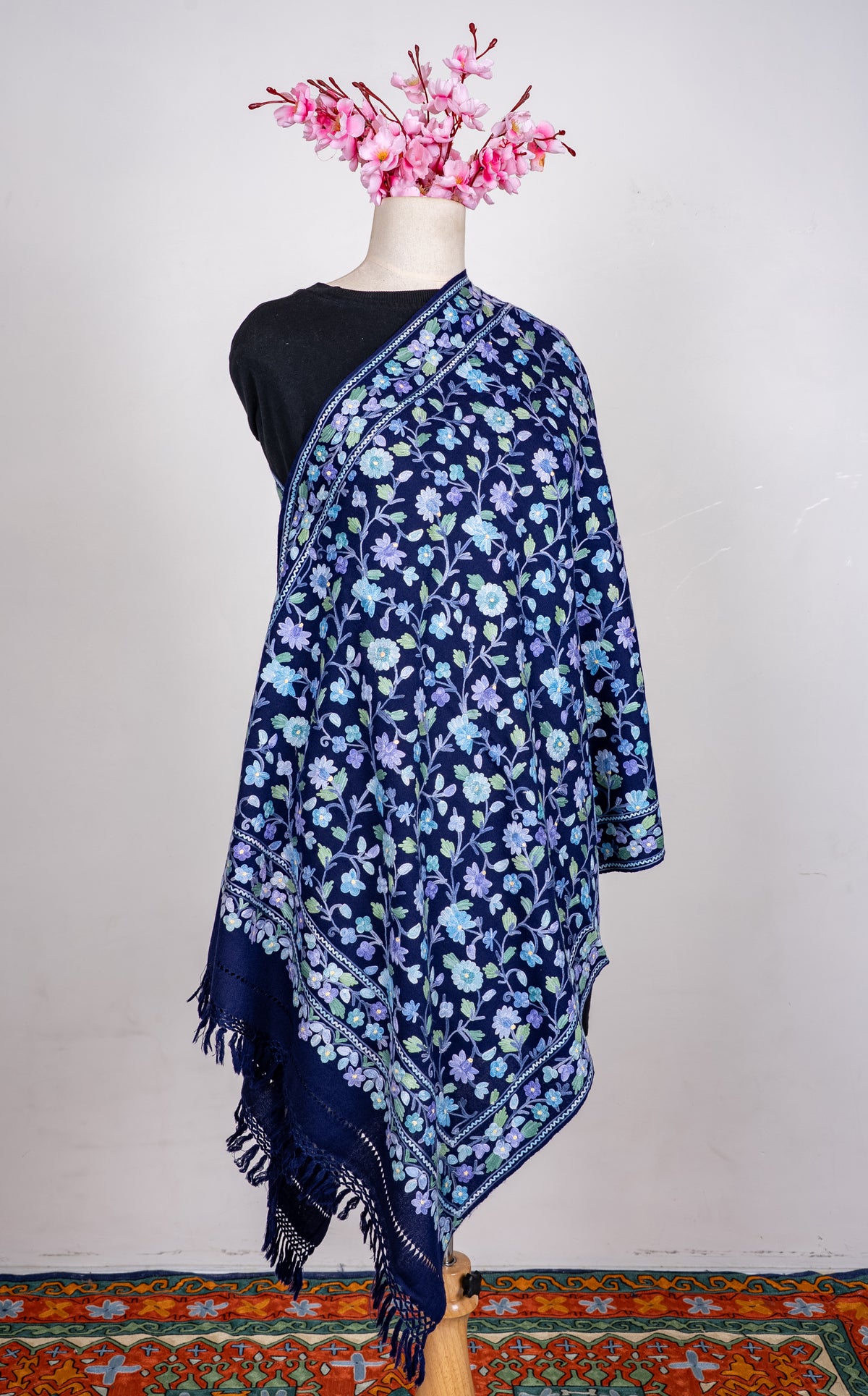 Full view of the sapphire-blue shawl on a mannequin, with all-over pastel Aari floral vines and a fringed end