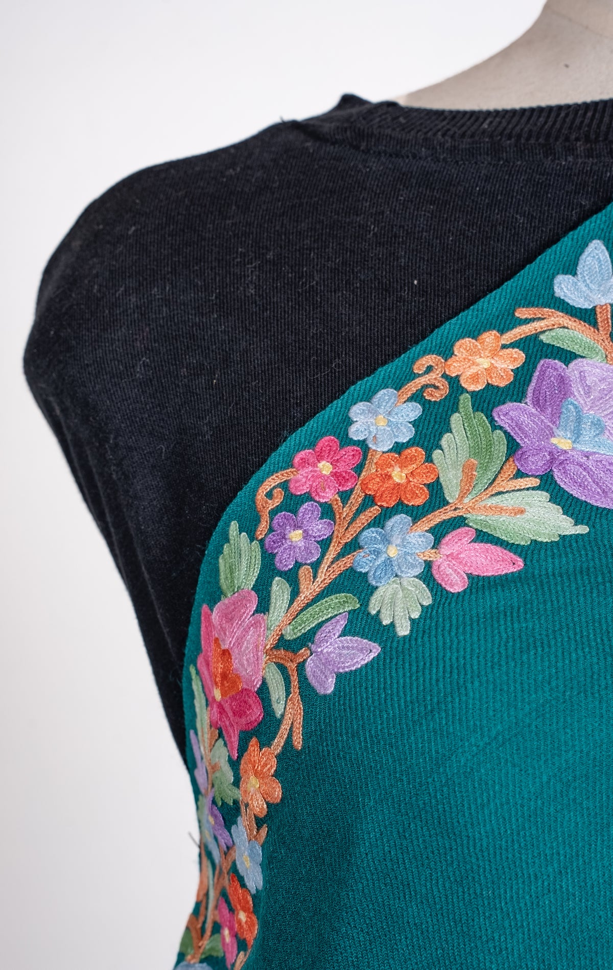 Close-up of a teal shawl across a mannequin's chest, with pink, peach, lavender and blue Aari flowers along the edge.