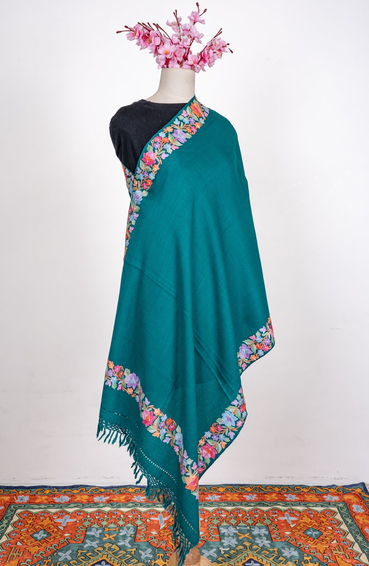 Teal shawl wrapped around a mannequin, with pastel Aari floral borders framing a plain centre and matching knotted fringe.