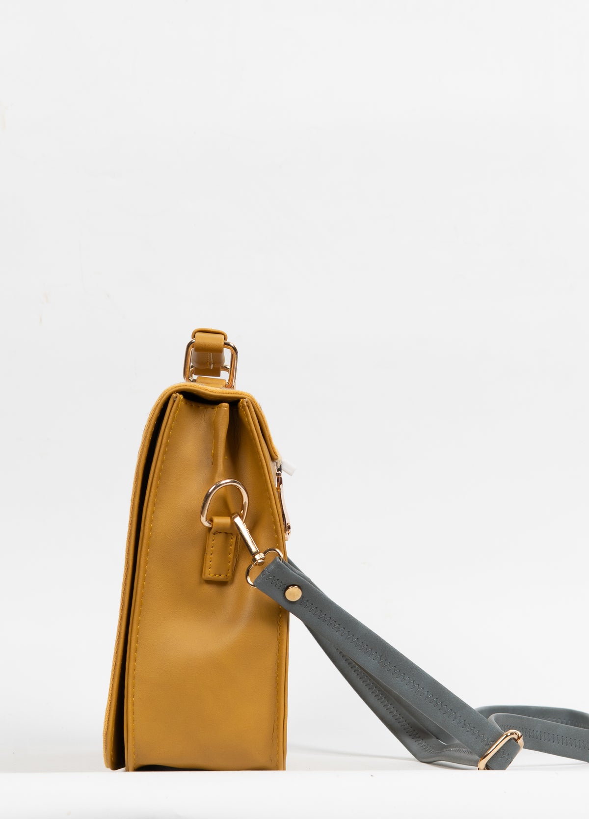 Side view of the structured mustard handbag, showing the gusset and grey strap clipped to a metal ring.