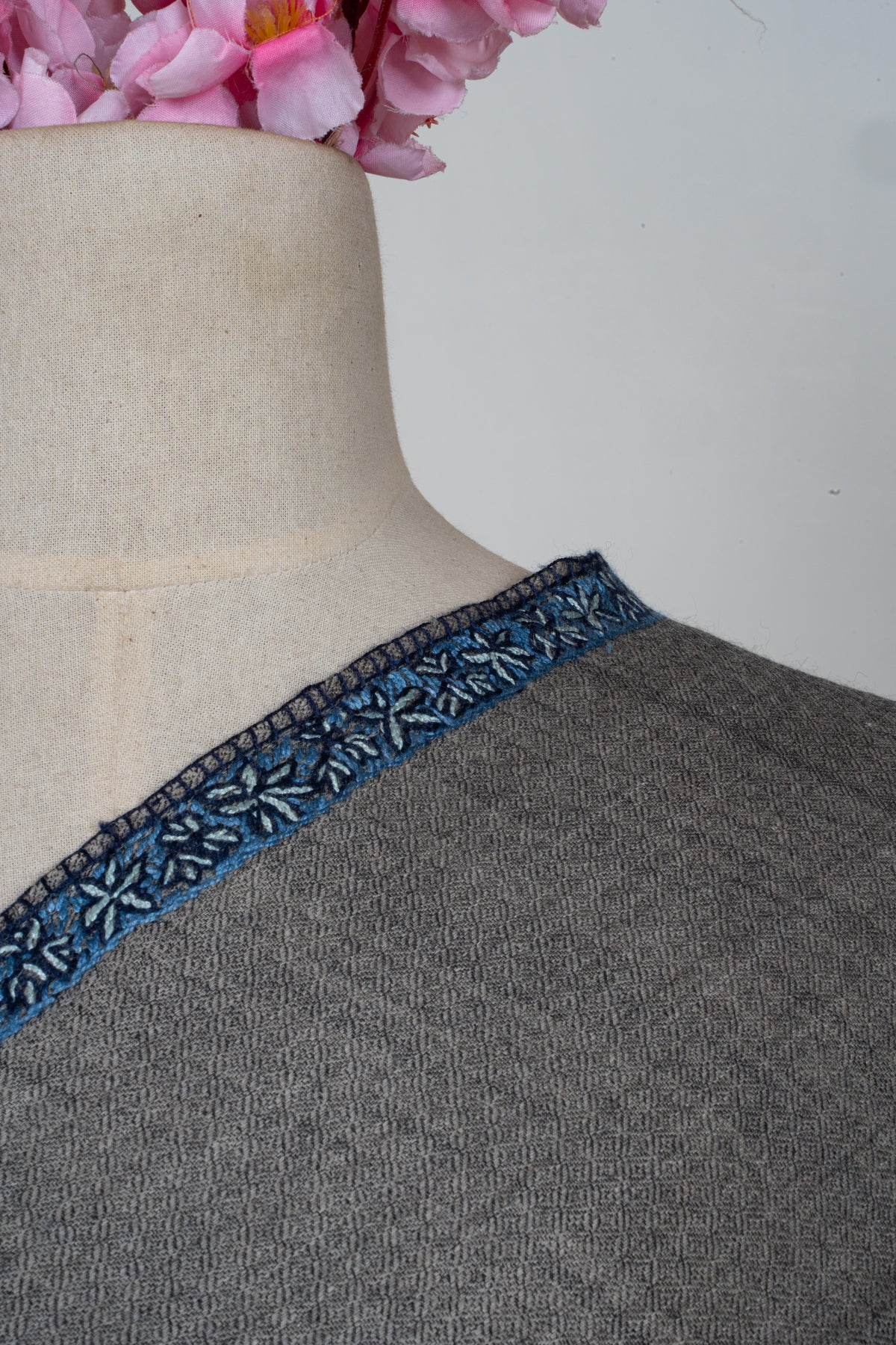Shoulder detail of pale-blue Sozni flowers and leaves on a dark blue border along a grey Merino wool shawl.