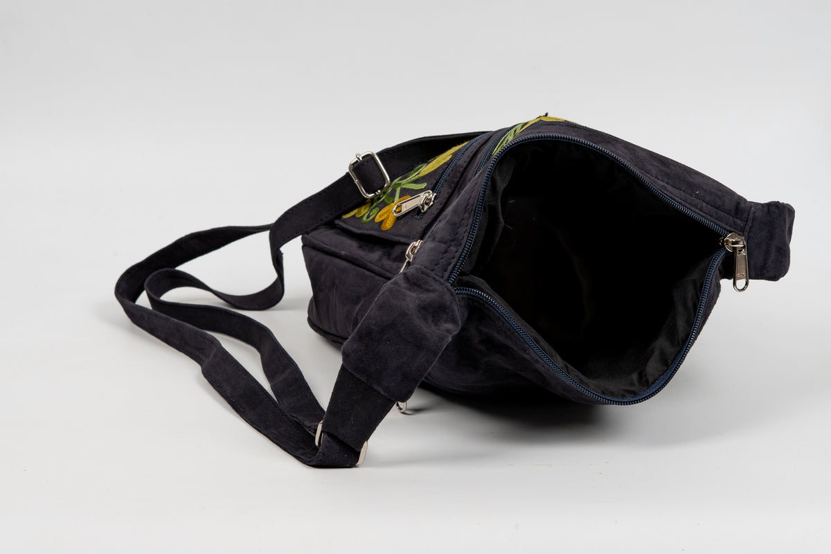 Black messenger bag laid on its side with the top zipper open, revealing the dark lining and interior space.