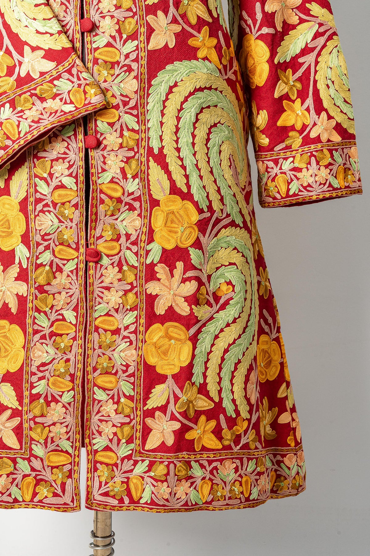 Lower front of the maroon jacket, showing yellow floral embroidery, green leafy swirls and a narrow patterned hem