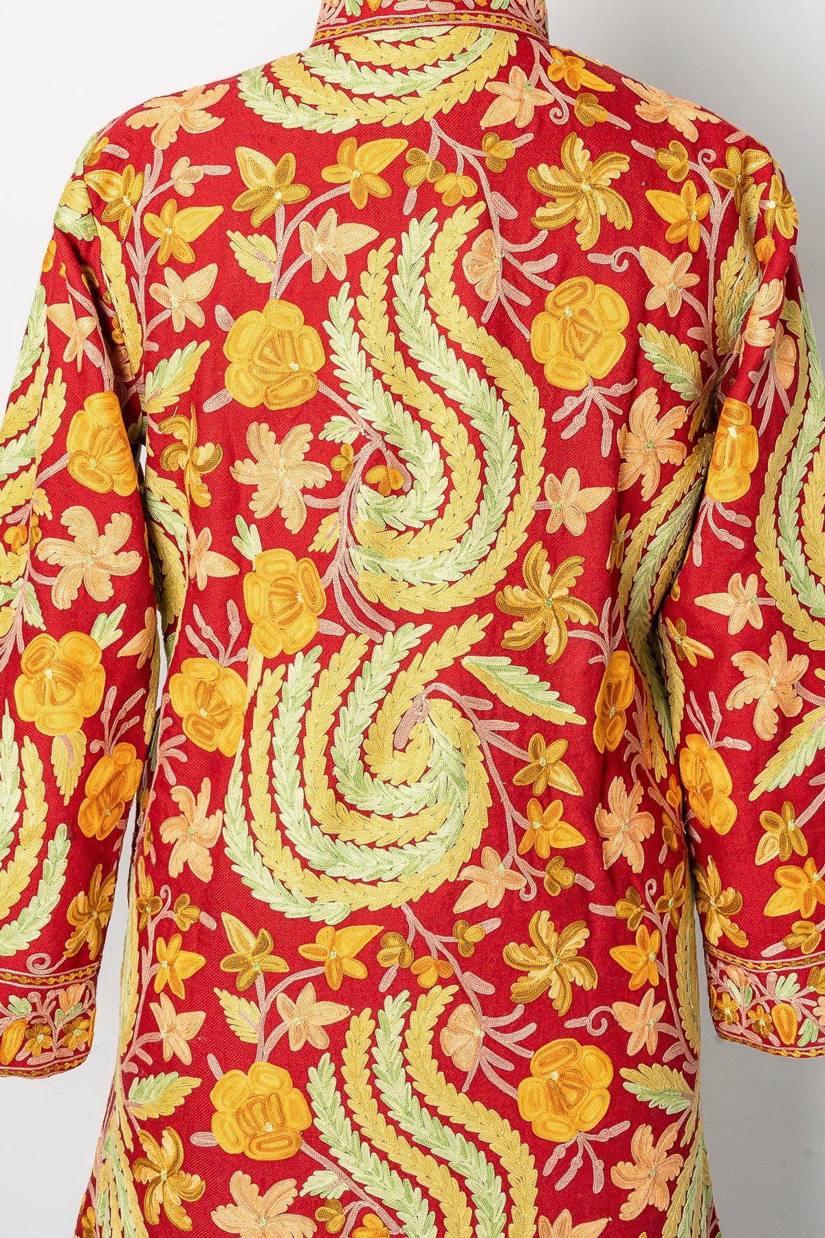 Upper-back detail of the maroon jacket, showing green leafy motifs, yellow flowers and fine curling stems