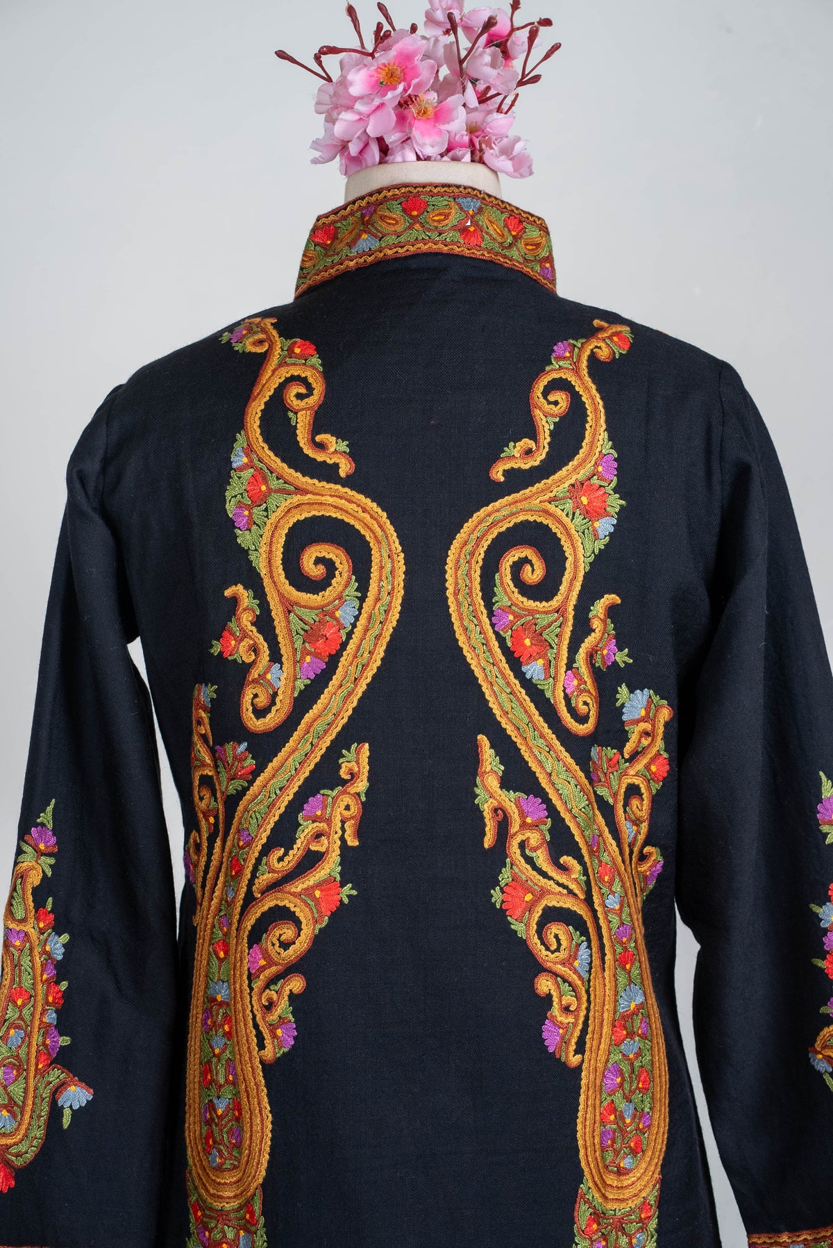 Upper-back view of the black short jacket, with mirrored golden-orange Aari scrolls and colourful floral accents