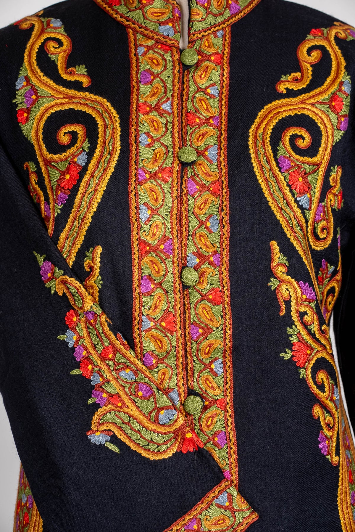 Close-up of the black jacket’s buttoned front and crossed sleeve, with golden-orange Aari scrolls and small multicoloured flowers