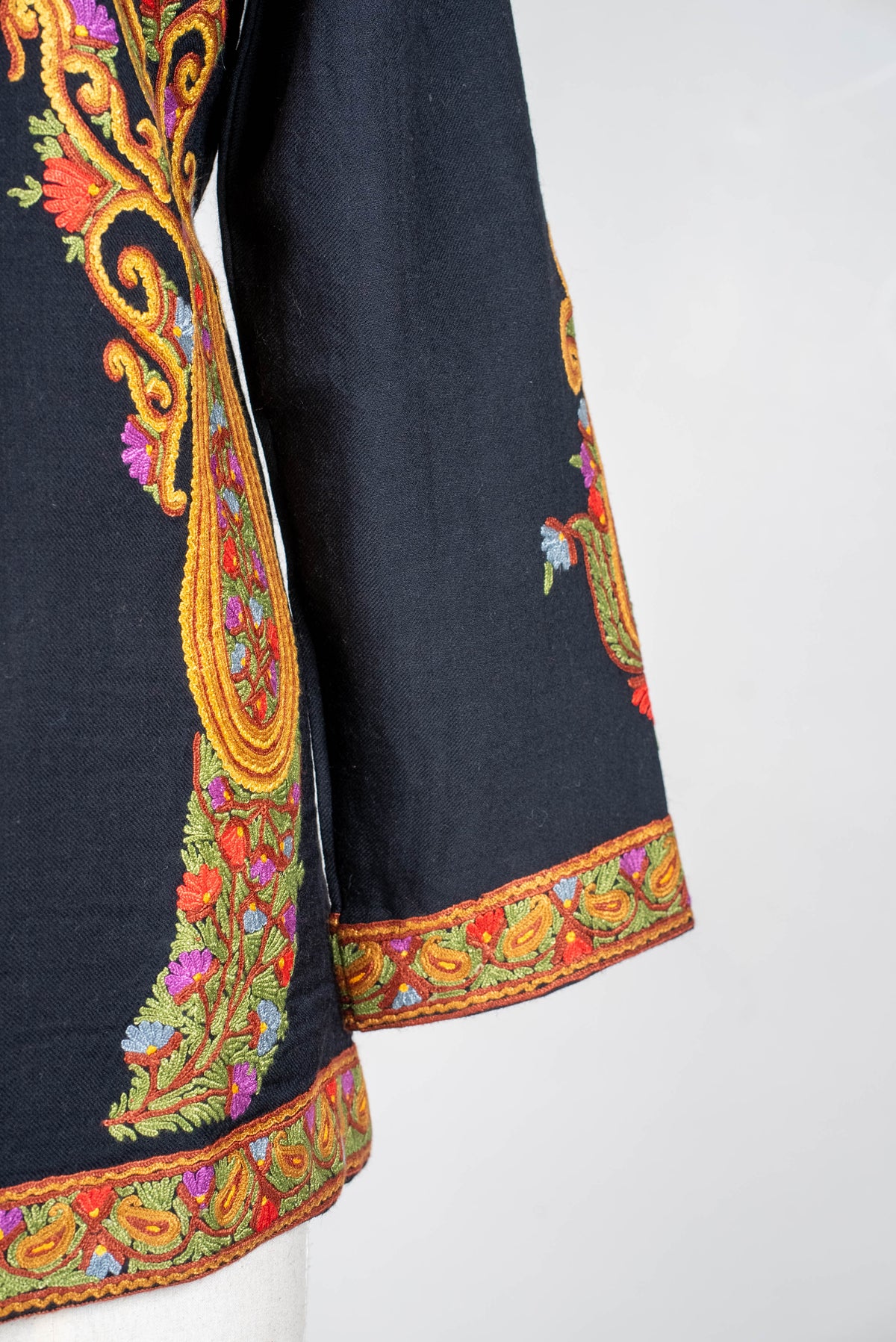 Sleeve and hem detail of the black short jacket, with golden-orange Aari scrolls and narrow multicoloured floral borders