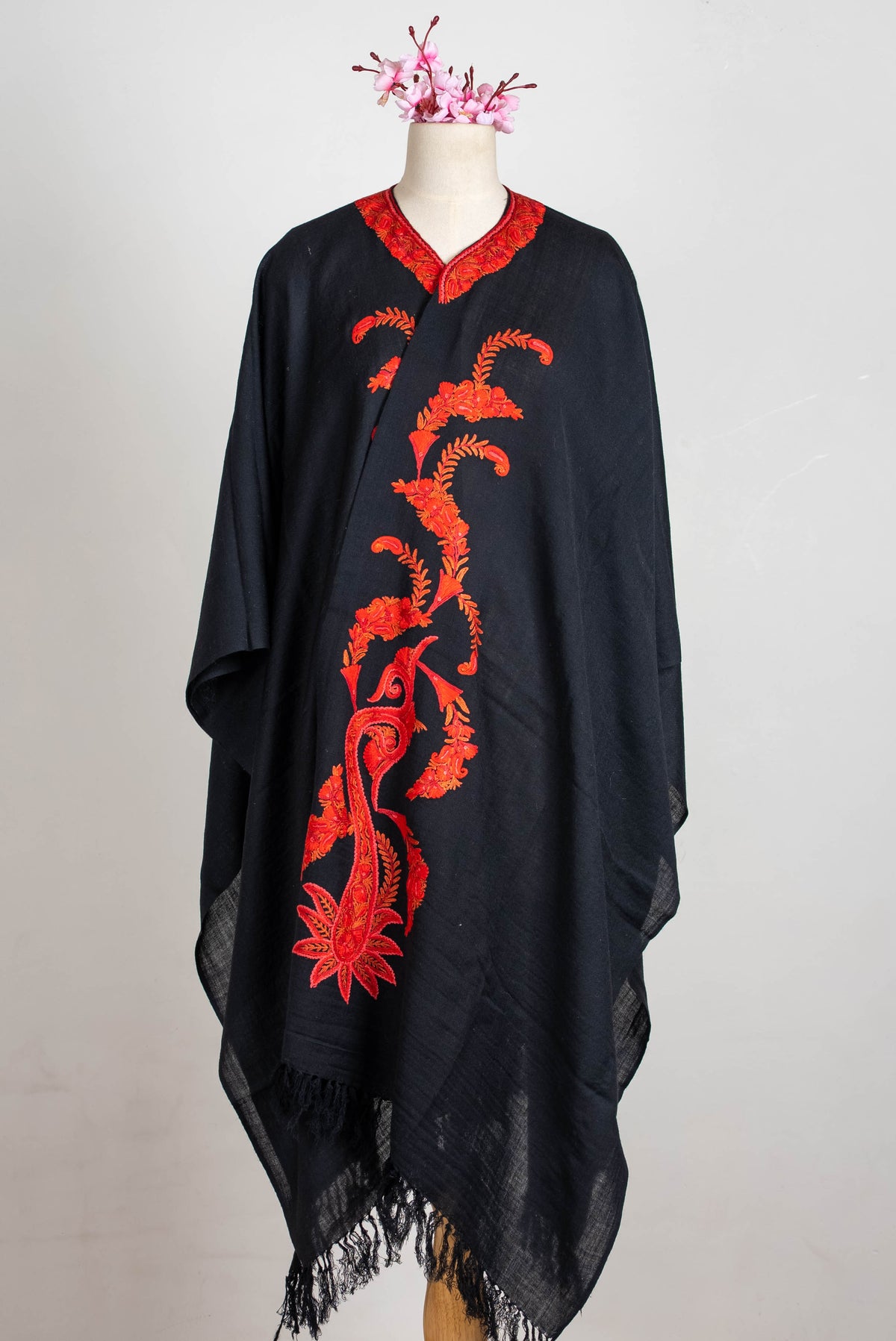 Full front view of a black shawl cape, with a long red-orange paisley and floral design and black fringe