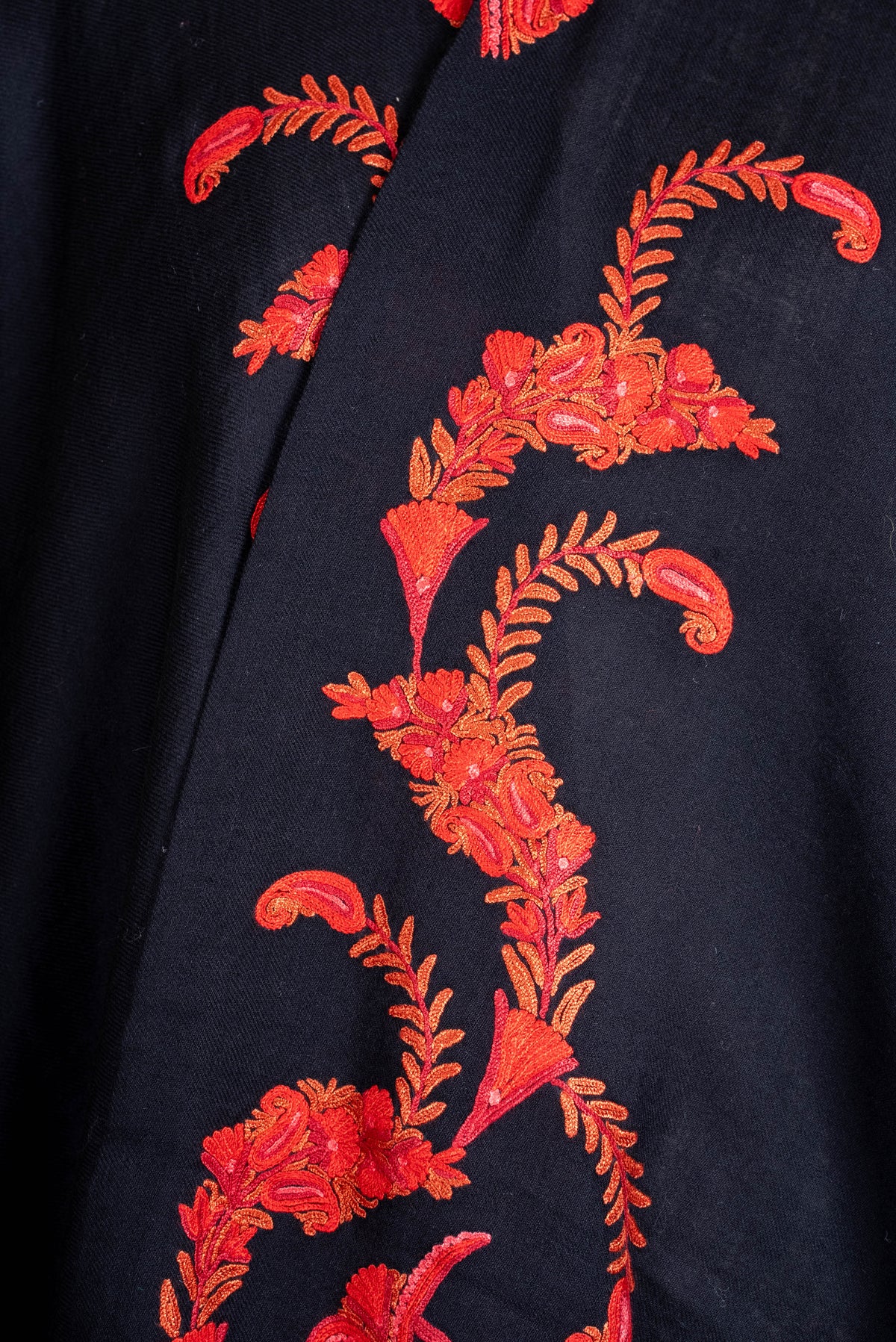Close-up of orange-red embroidered flowers and curved leafy stems on the black cape's front