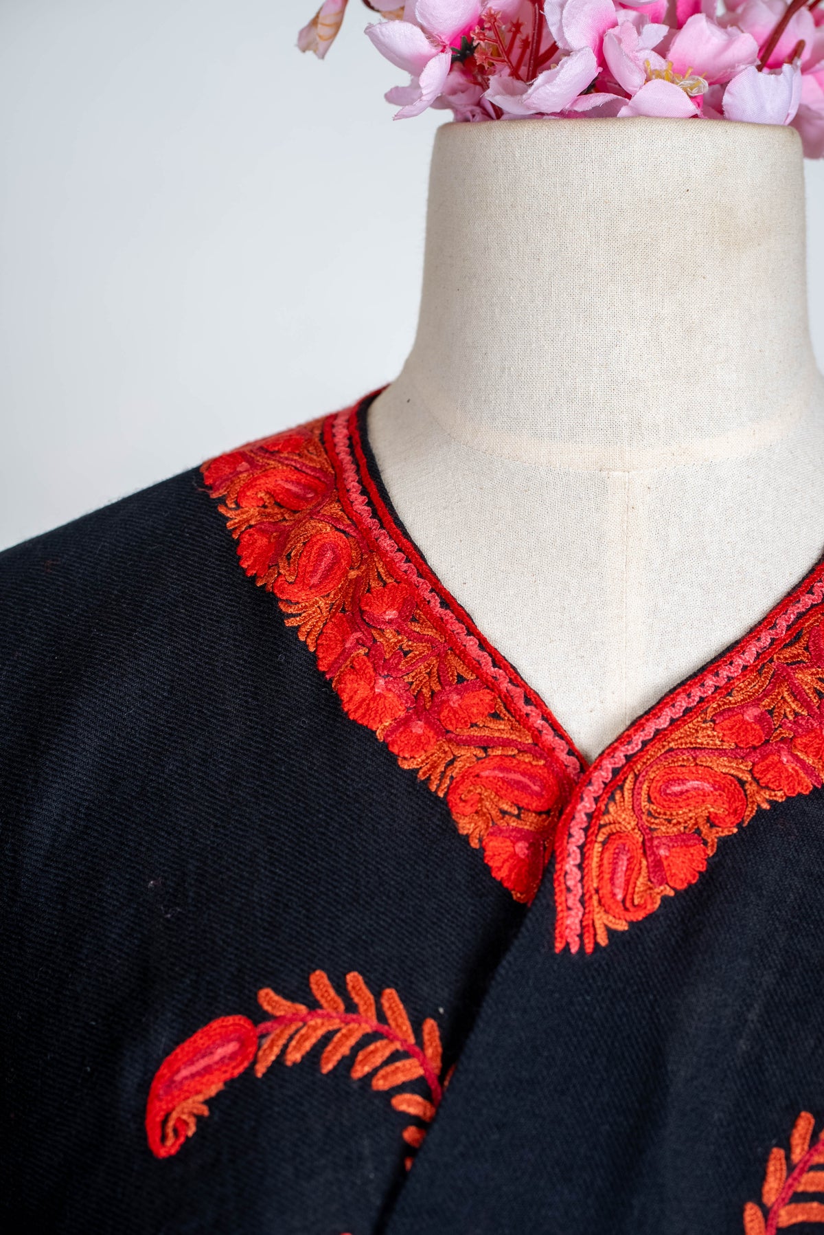 Close detail of the black cape's curved neckline, with dense red-orange leaf embroidery