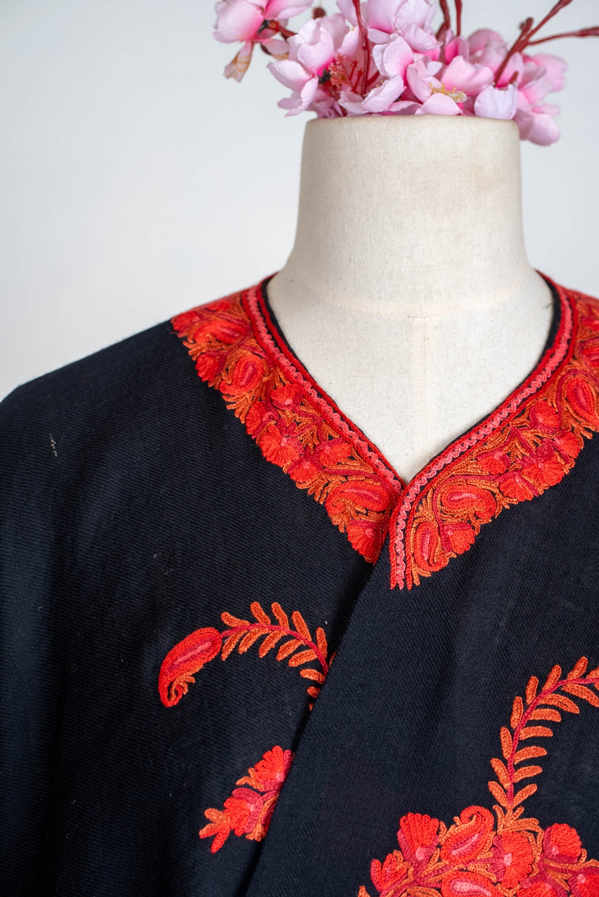 Upper-front view of the black cape, showing the red embroidered neckline above curved orange-red stems