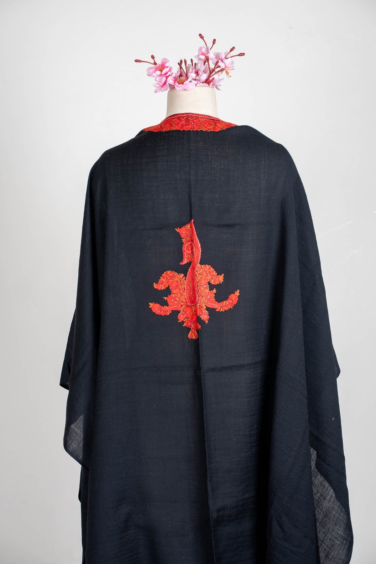 Angled back view of the black cape, with a central red-orange motif and plain loosely draped sides