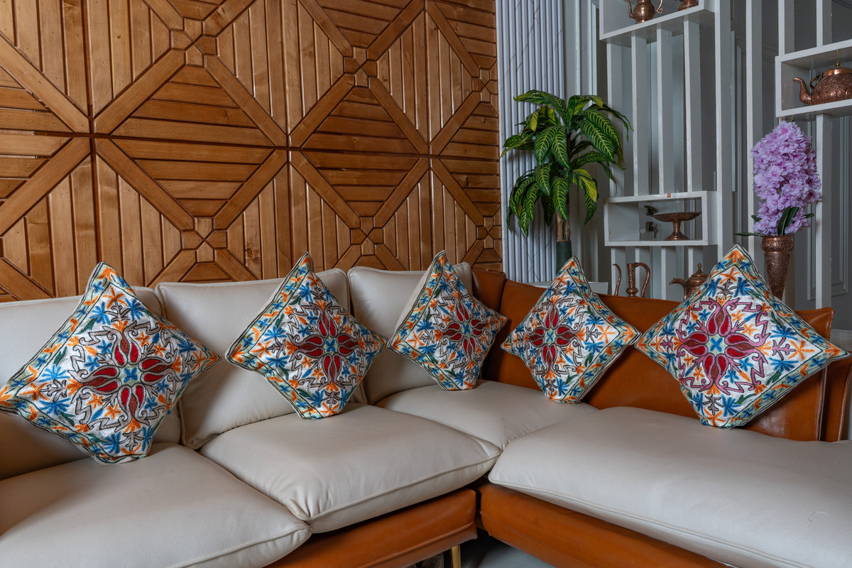 Five matching ivory cushions with red, blue and orange floral embroidery arranged across a cream corner sofa
