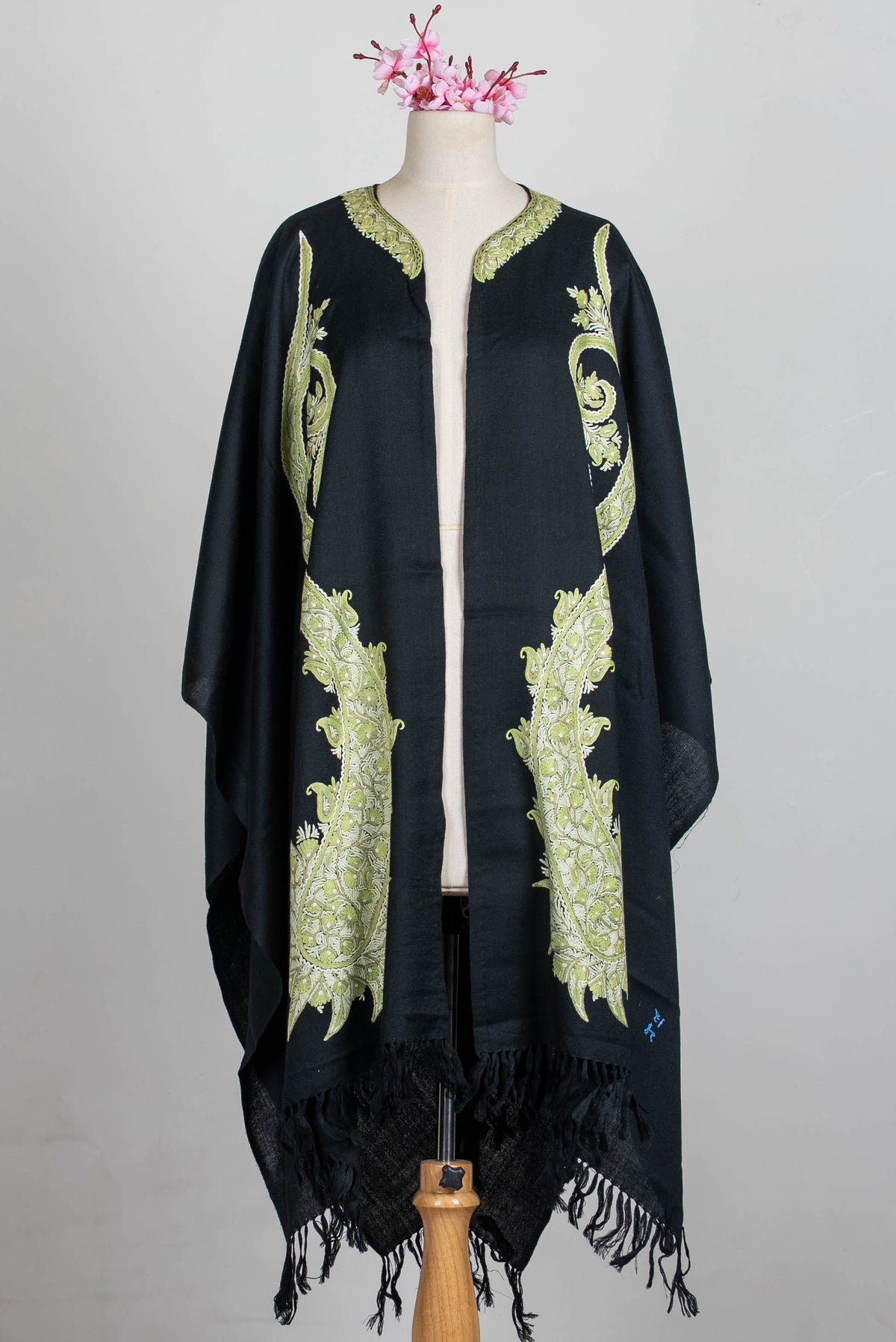 Full open-front view of the black cape on a mannequin, with paired elongated sage-green paisleys and black fringe