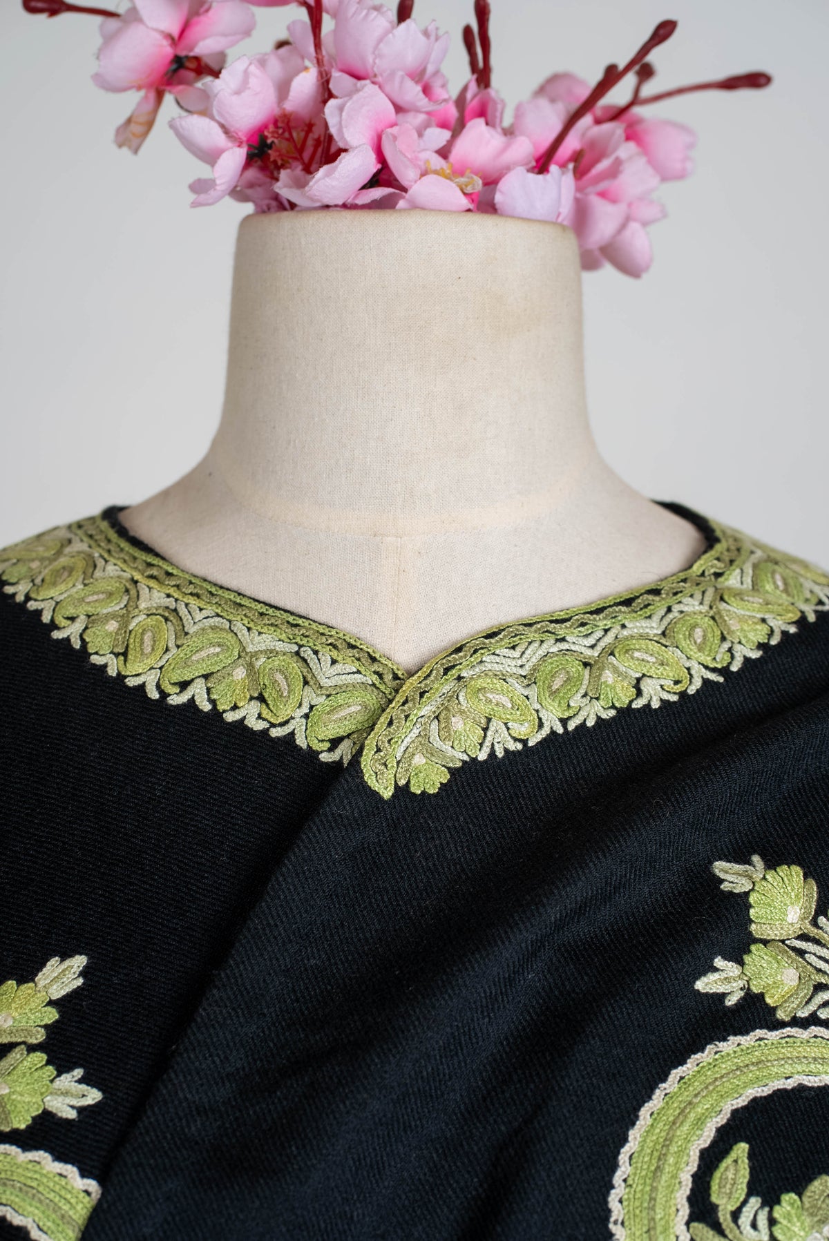 Tight neckline detail of the black cape, showing sage-green embroidered leaves outlined in ivory