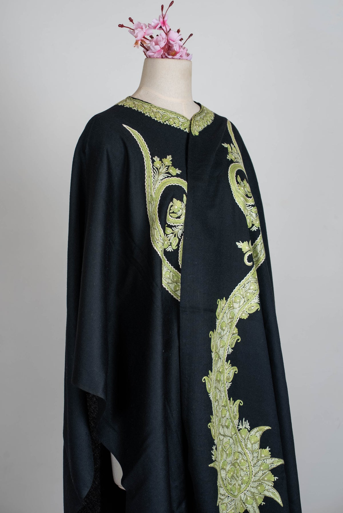 Angled upper-body view of the black cape wrapped across a mannequin, with sage-green paisley embroidery