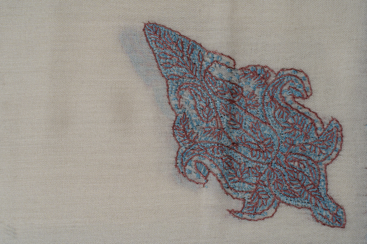 Close-up of a turquoise and coral Sozni floral motif with curled lobes on ivory fabric