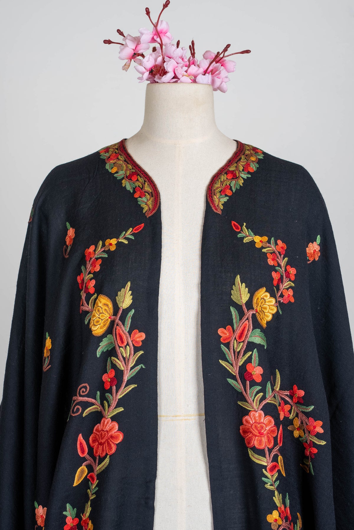 Upper open-front view of the black shawl cape, with coral, orange and green embroidered floral vines along both panels