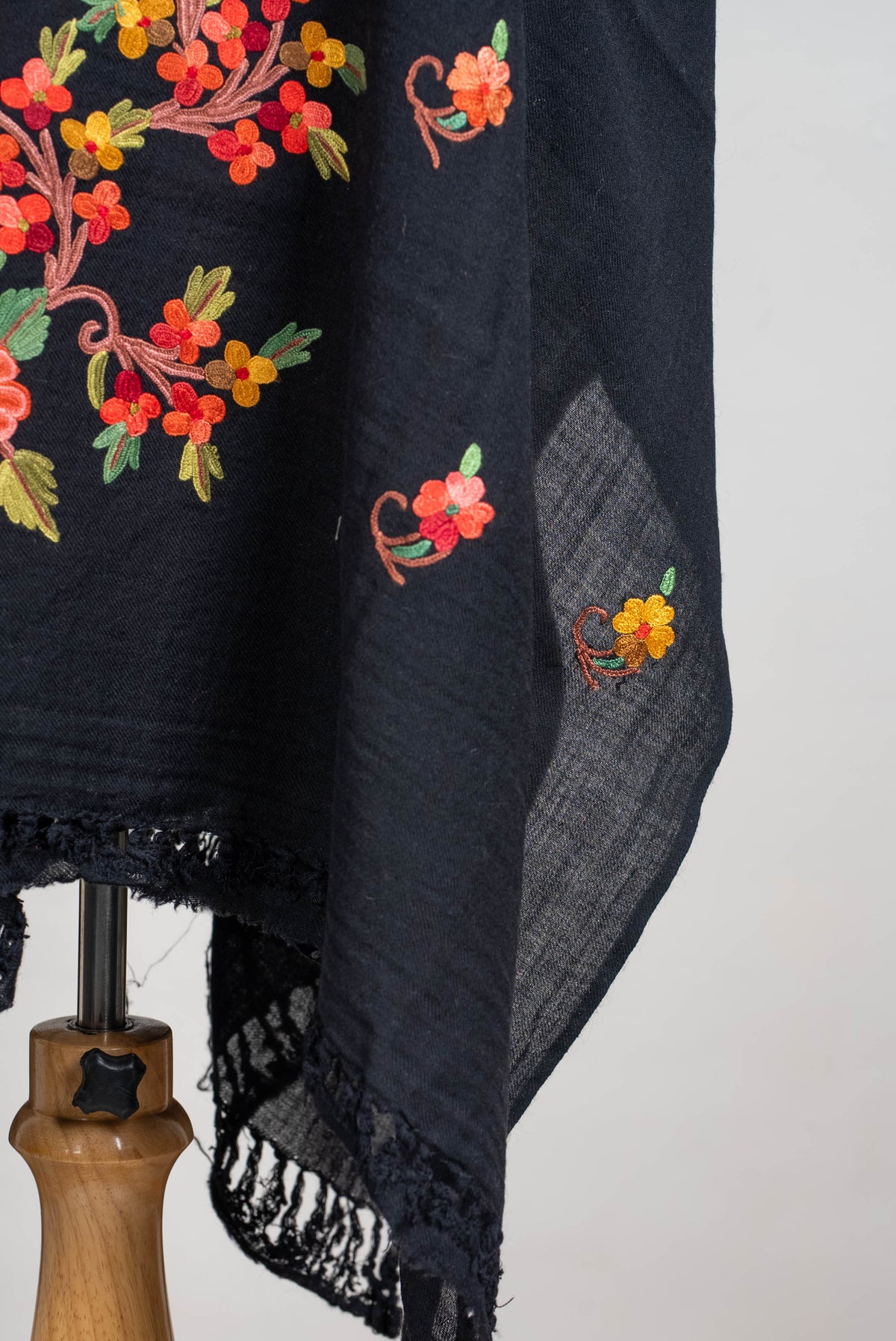 Lower-edge detail of the black shawl cape, with small coral and yellow floral motifs, lightweight folds and black fringe