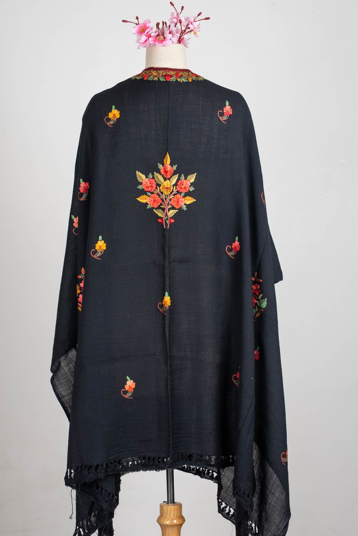 Back view of the black shawl cape on a mannequin, with a central coral and yellow floral bouquet, scattered sprigs and fringe