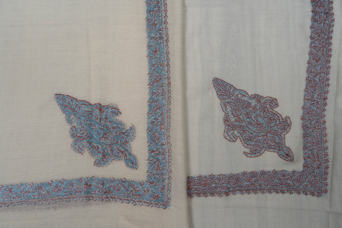 Overlapping ivory rumal corners showing both sides of turquoise and coral Sozni motif and border stitching